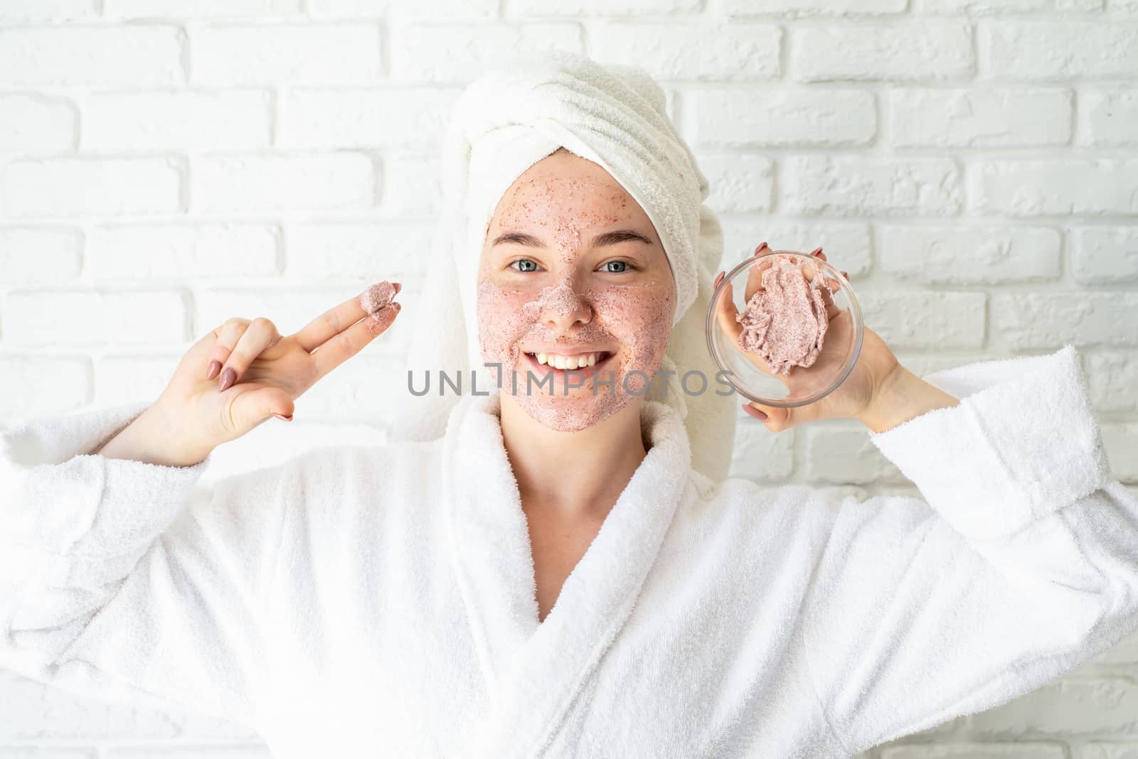 Happy young woman applying face scrub on her face by Desperada