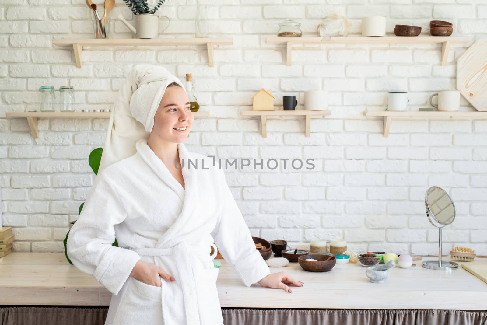 Happy young woman applying face scrub on her face in her home kitchen by Desperada