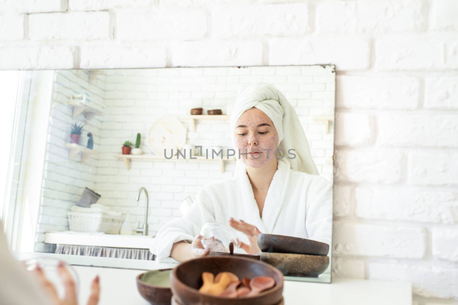 Happy young woman applying face scrub on her face by Desperada