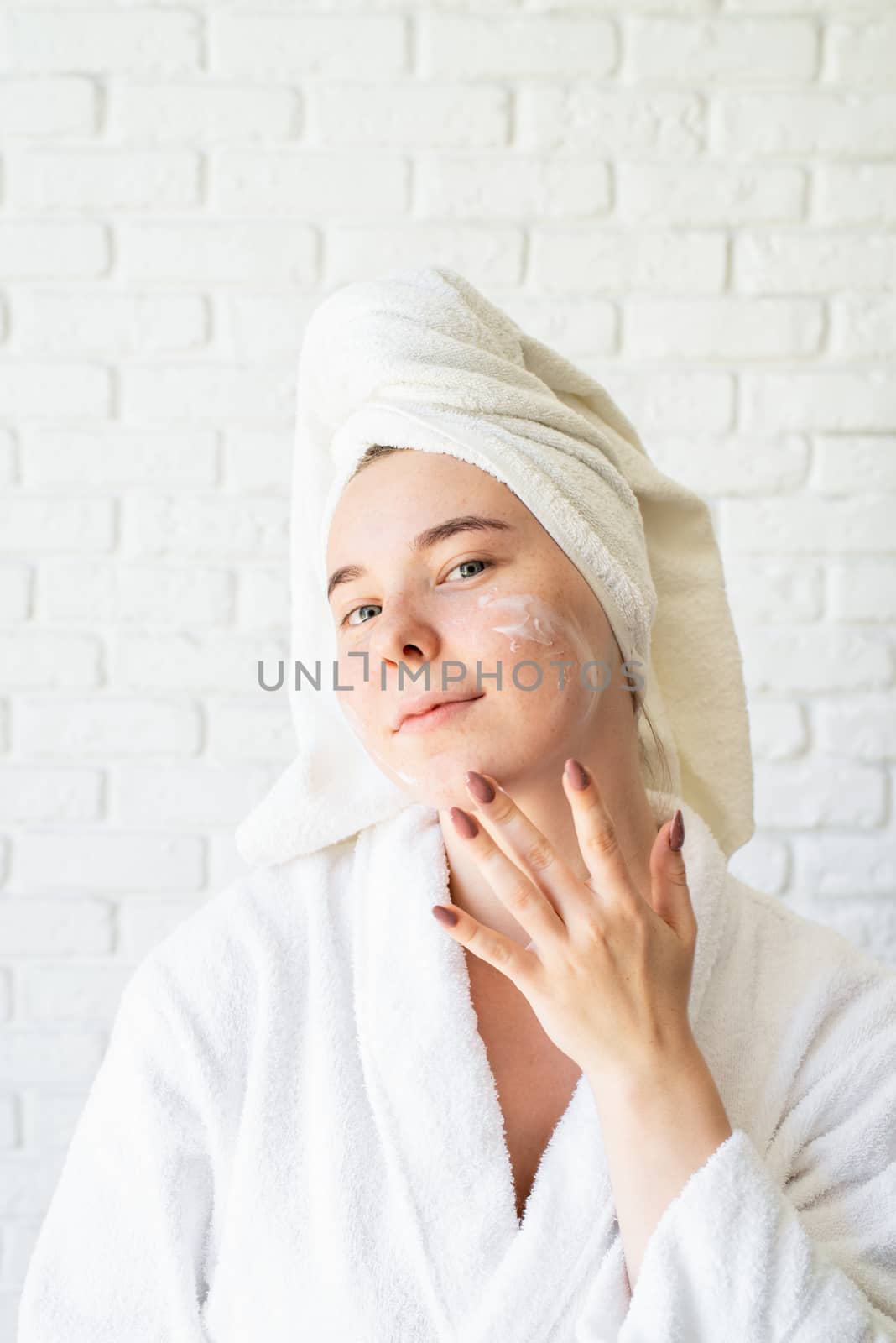 Spa and wellness. Natural cosmetics. Self care. Happy young caucasian woman in white bath towel applying face cream at home