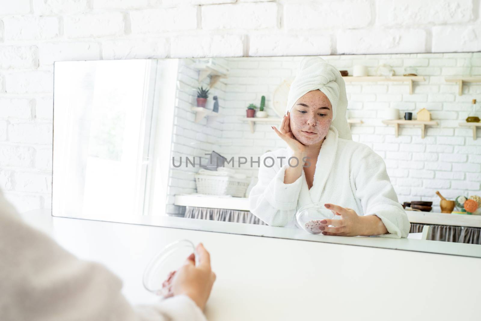 Happy young woman applying face scrub on her face by Desperada