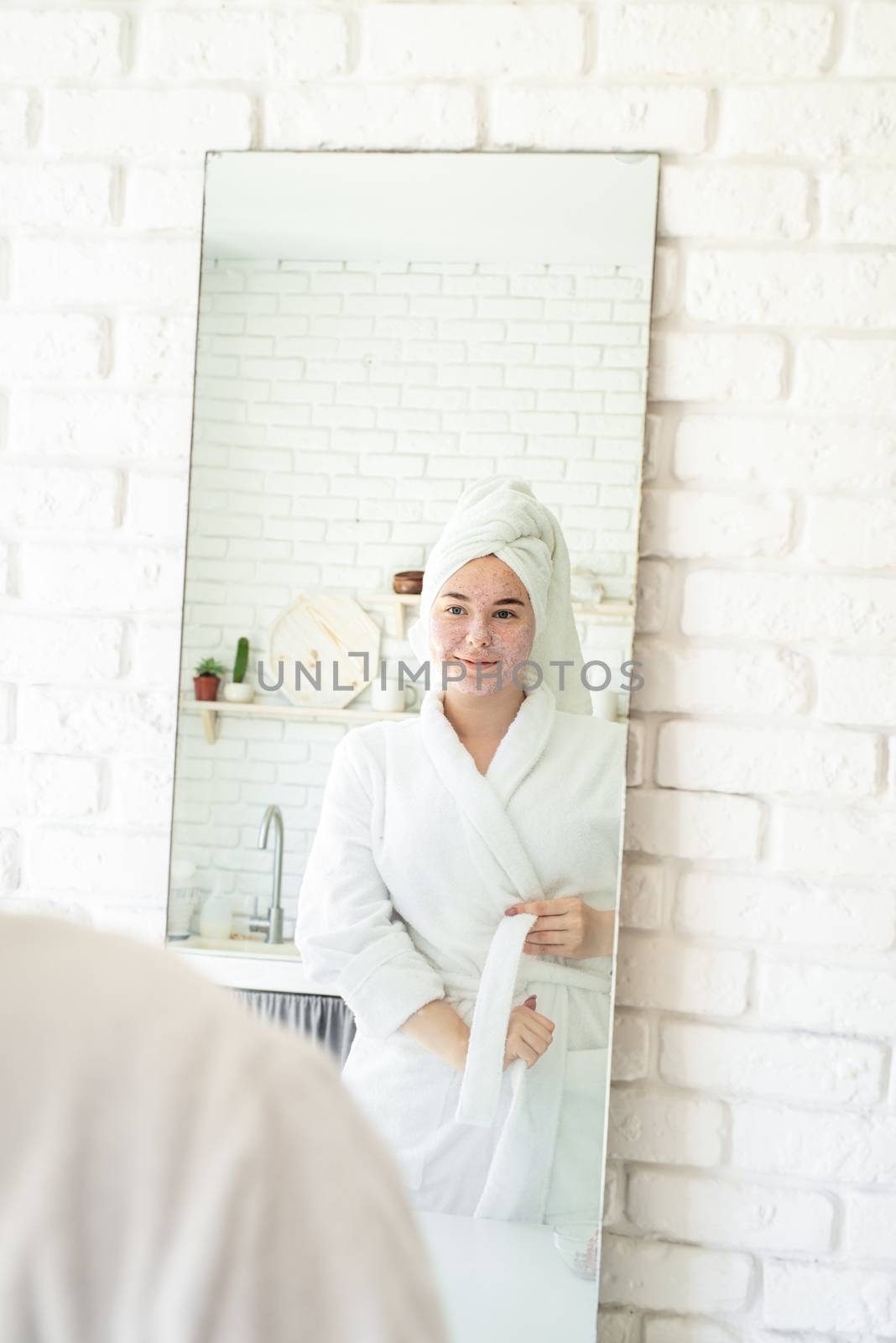 Happy young woman applying face scrub on her face by Desperada