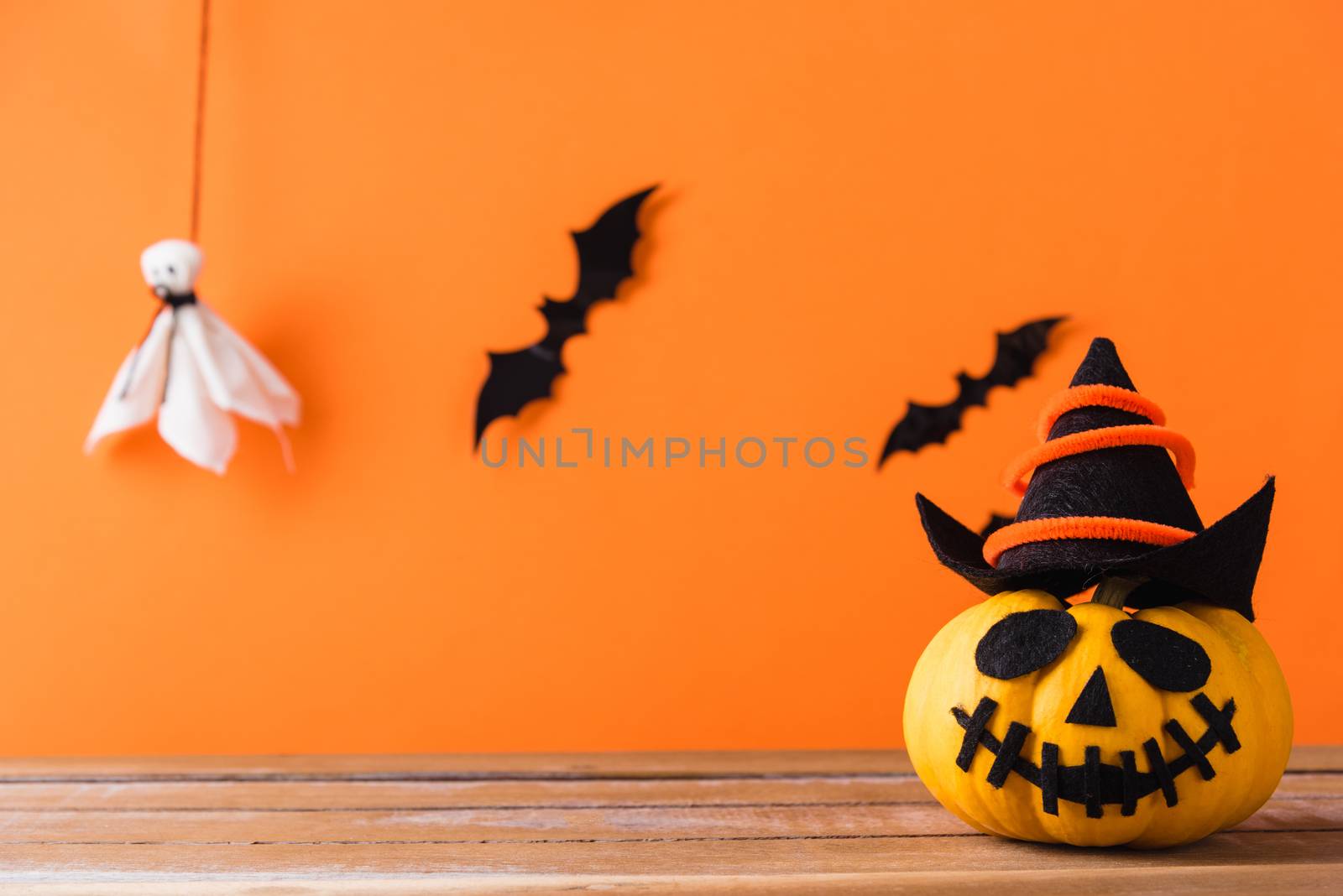 Funny Halloween day decoration party, Cute pumpkin ghost spooky jack o lantern face wear hat, black spider and bats on wooden table, studio shot isolated on an orange background, Happy holiday concept