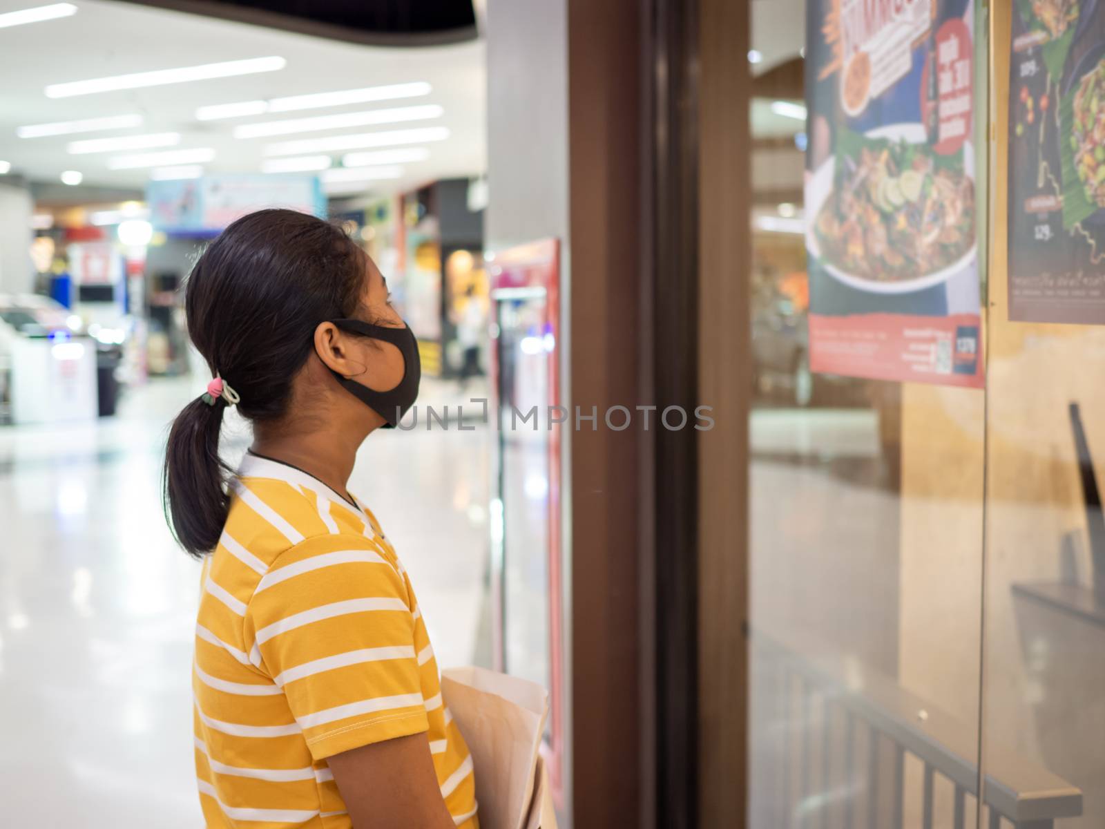 A woman wearing a mask in a shopping mall And looking at the sign in front of the restaurant.