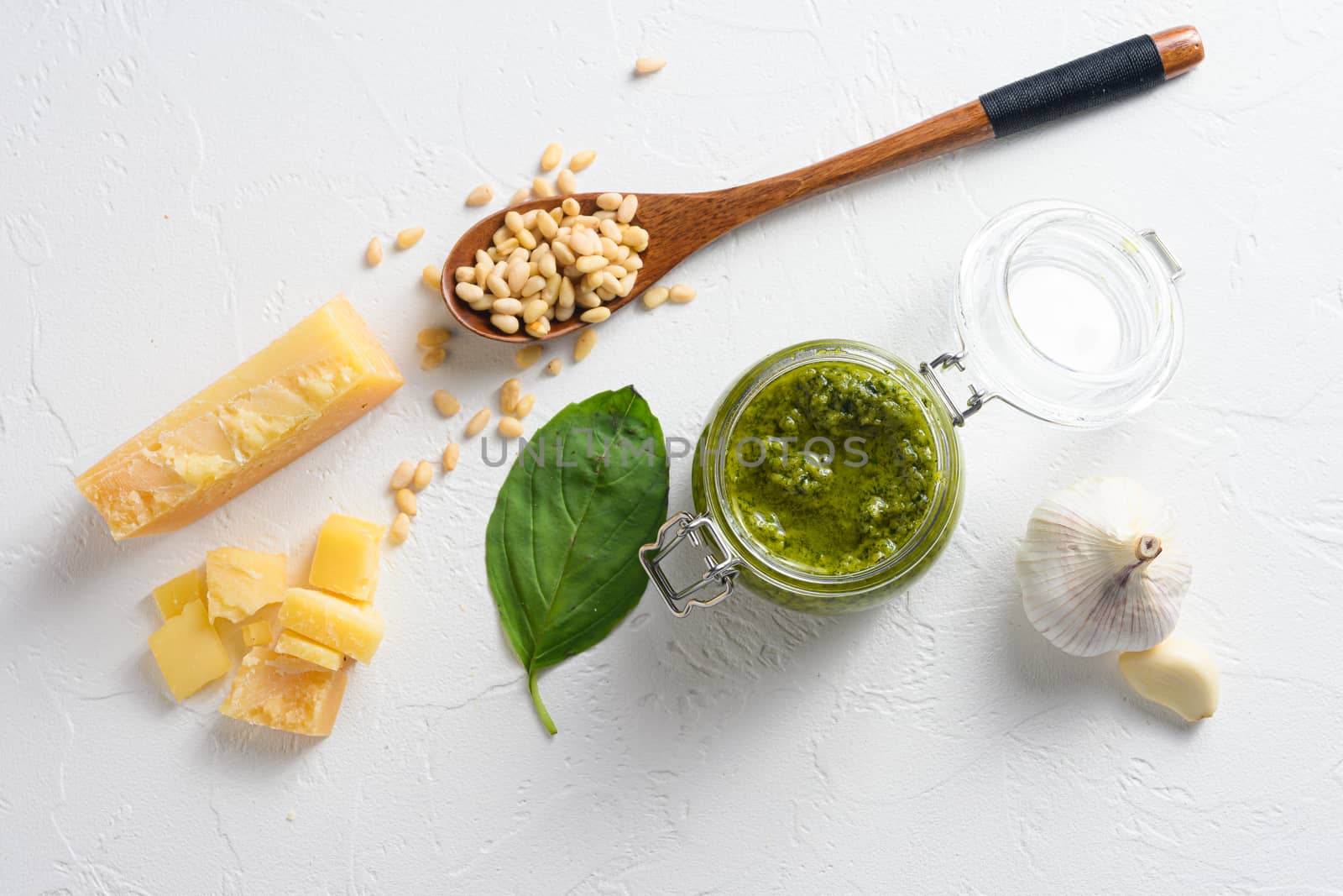 classic Basil pesto sauce in a glass jar. fresh basil leaves, grated parmesan cheese, pine nuts, garlic, white table concrete from above top view.