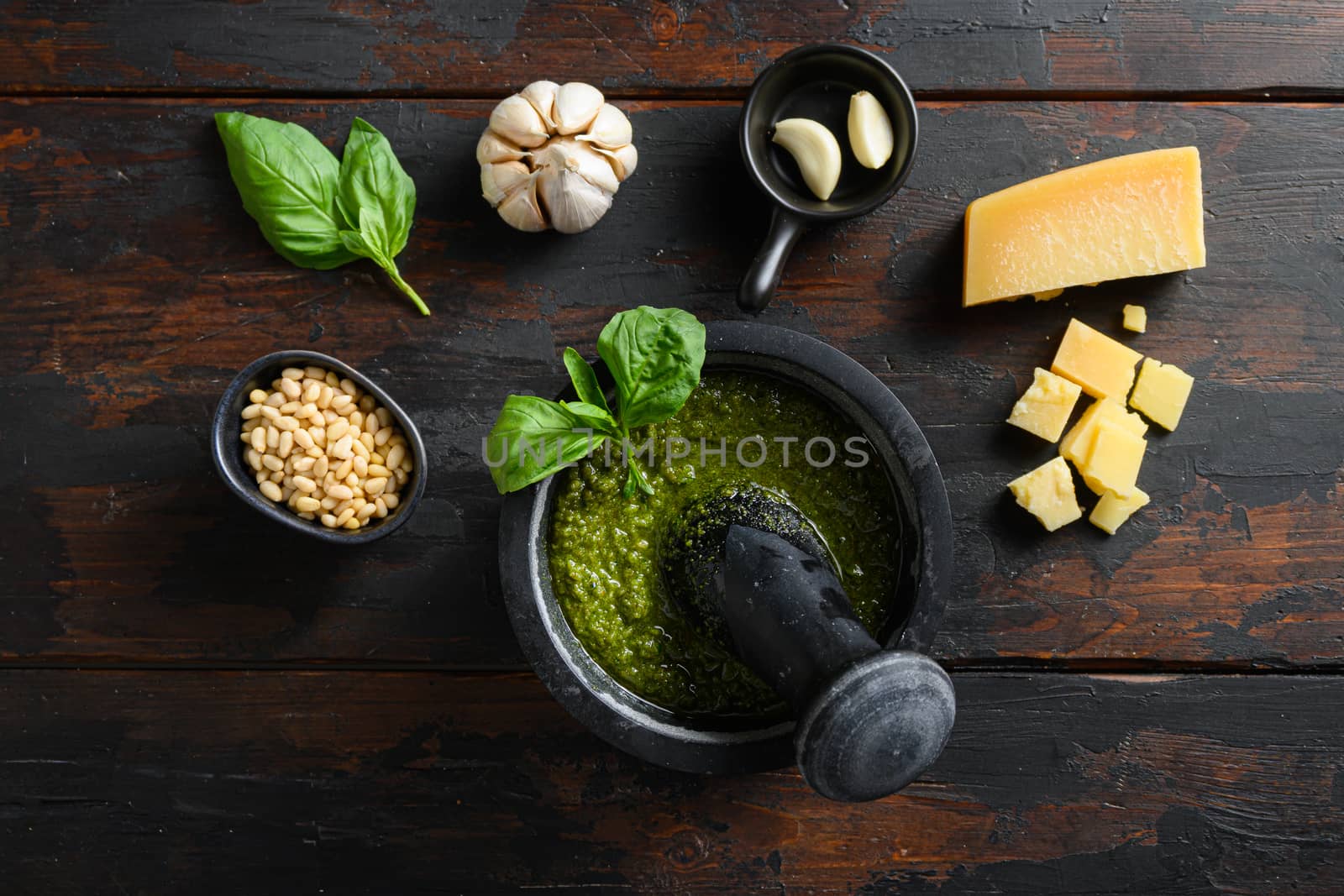 fresh Green basil pesto in mortar preparation in black mortar with italian recipe ingredients over old wood table overhead