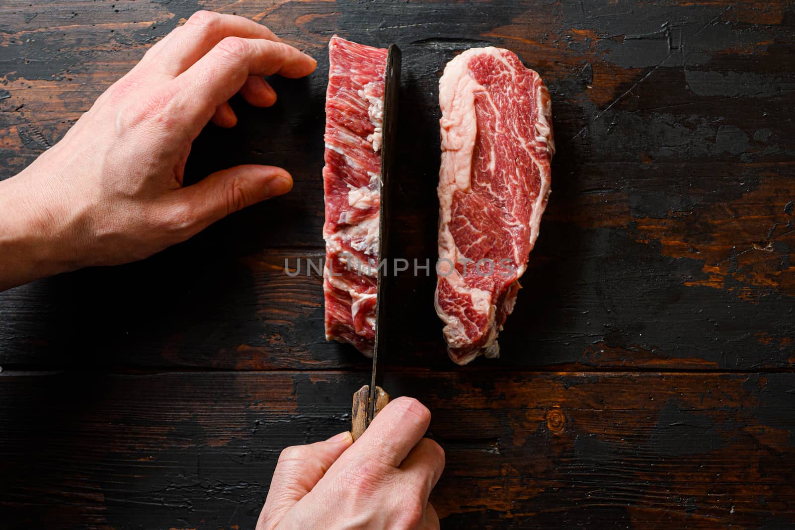 Raw Chuck eye roll black angus marbled beef steak on vintage dark wood table Organic beef. with butcher hands and meat cleaver at work chop.