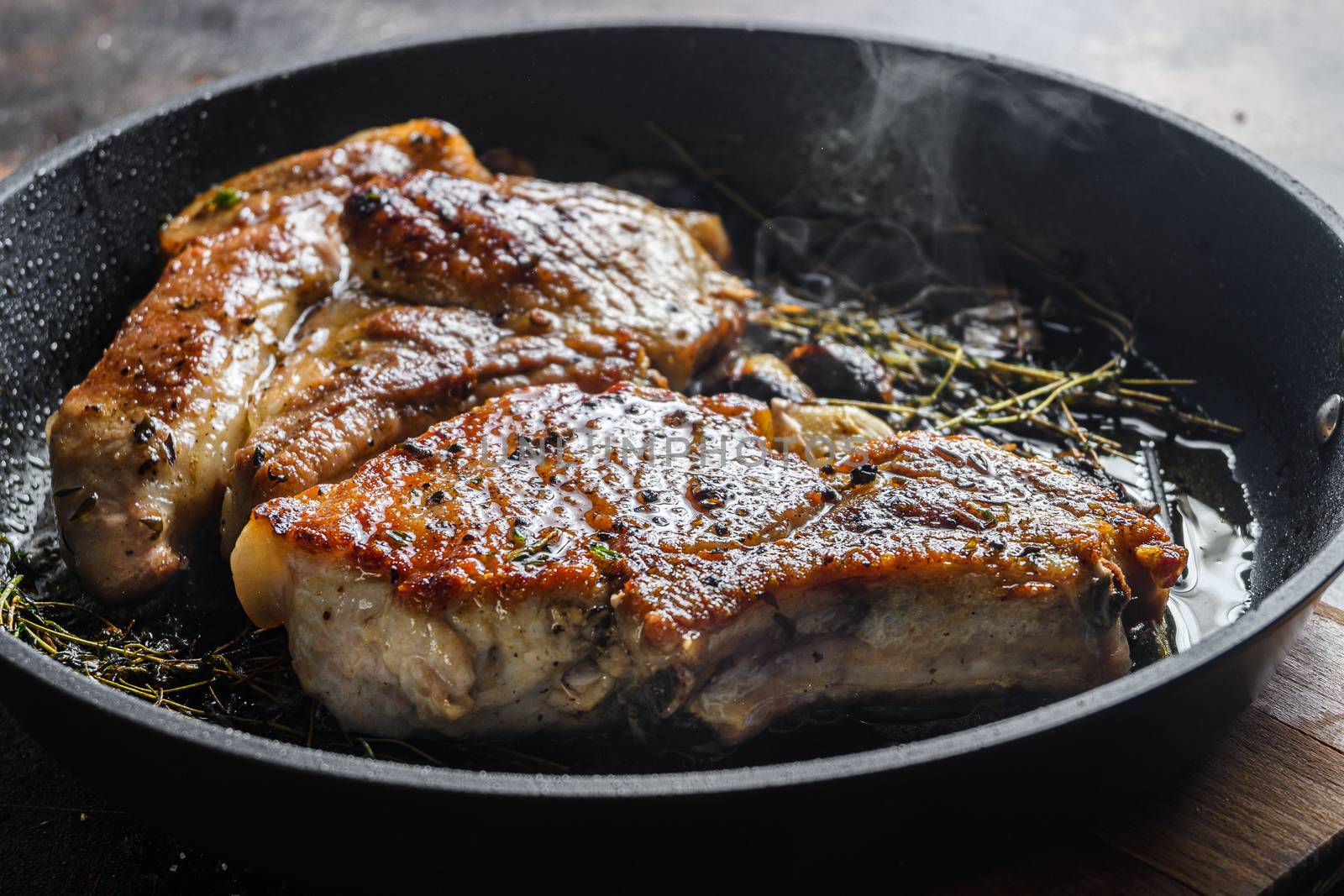 Grilled pork steak on the bone with seasonings on hot pan with smoke side view close up horisontal