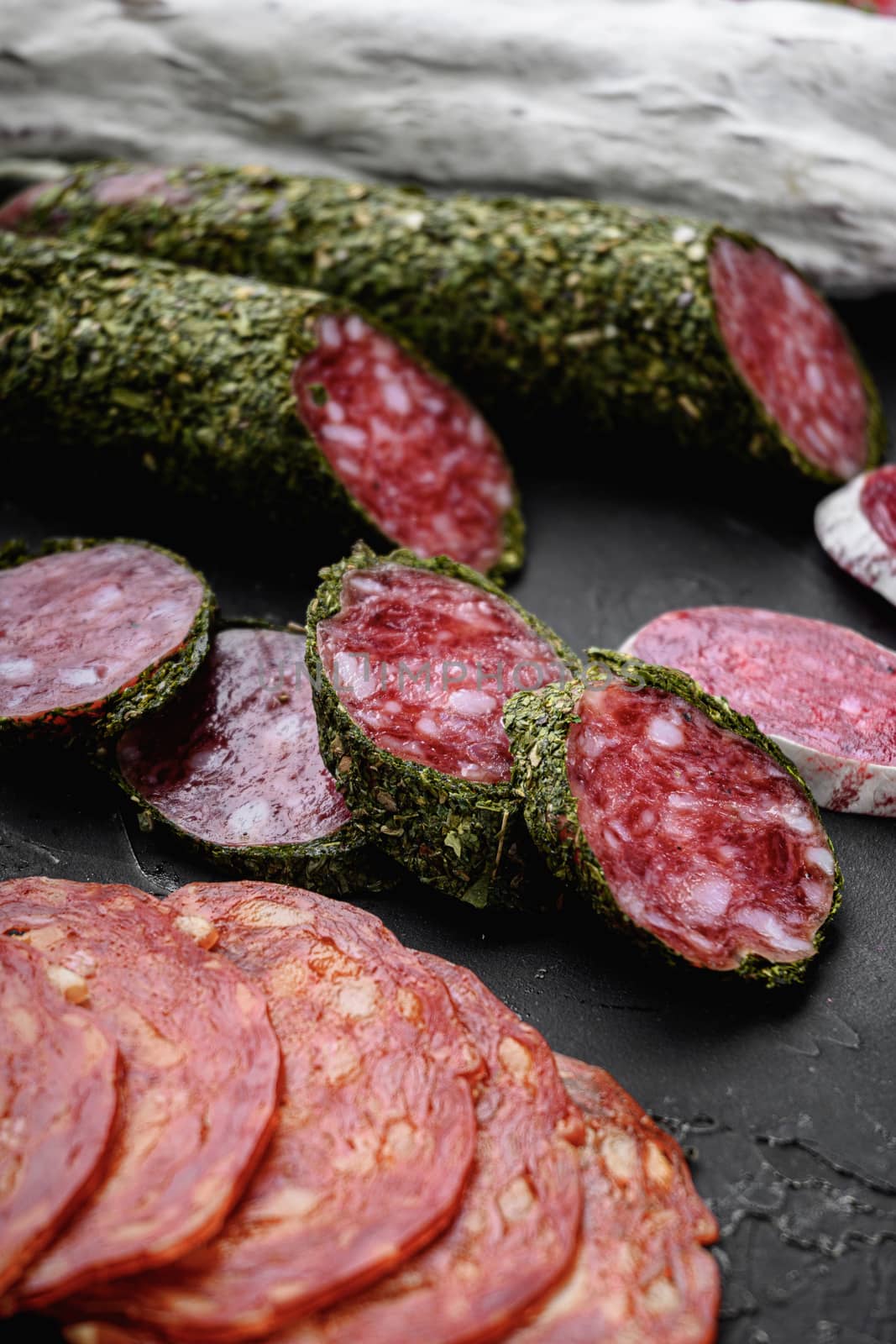 Set of dry cured salami, spanish sausages, slices and cuts on black textured surface.