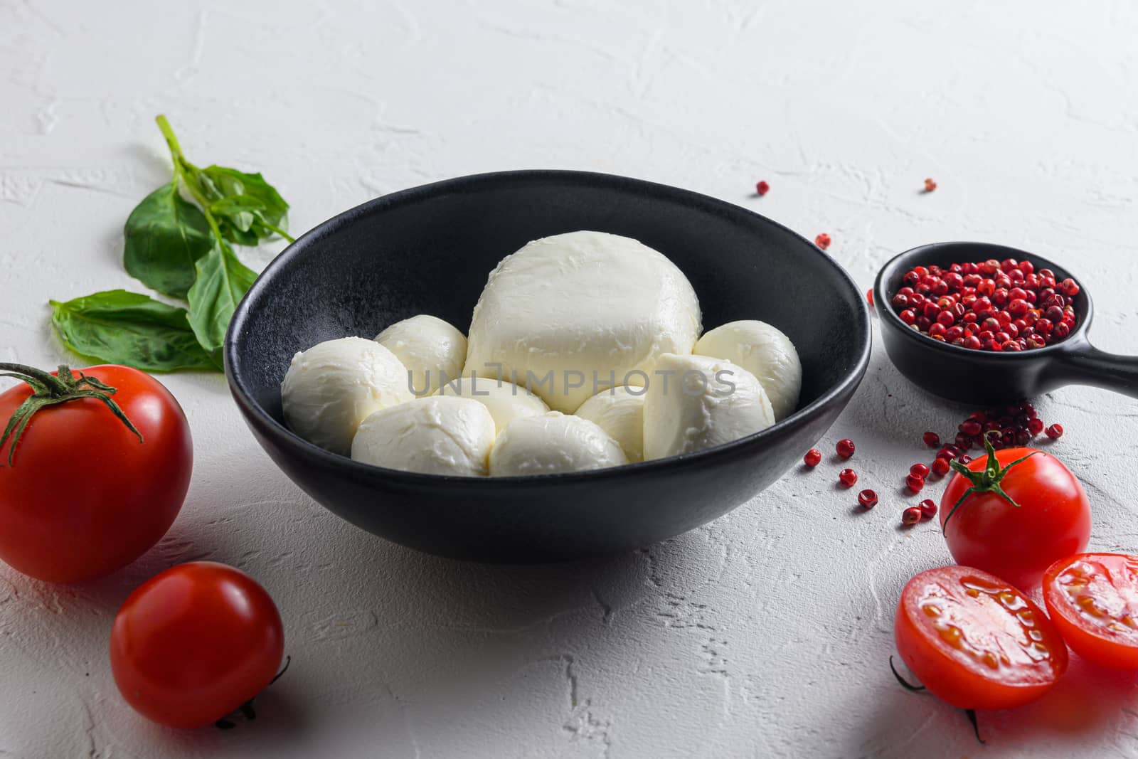 Mozzarella cheese in black bowl, basil tomato cherry balsamic black slate stone copy space. Ingredients for Caprese salad on white background close up selective focus.