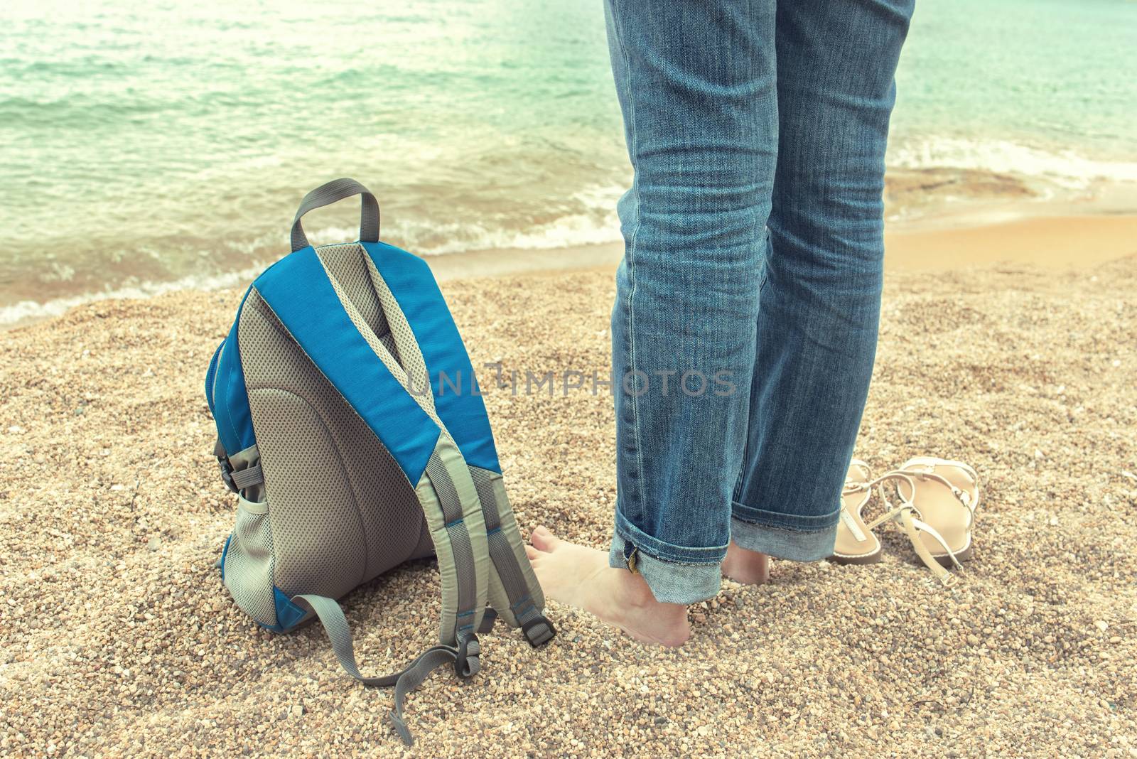 Goodbye summer concept. Girl is standing by the sea. Backpack in the sand