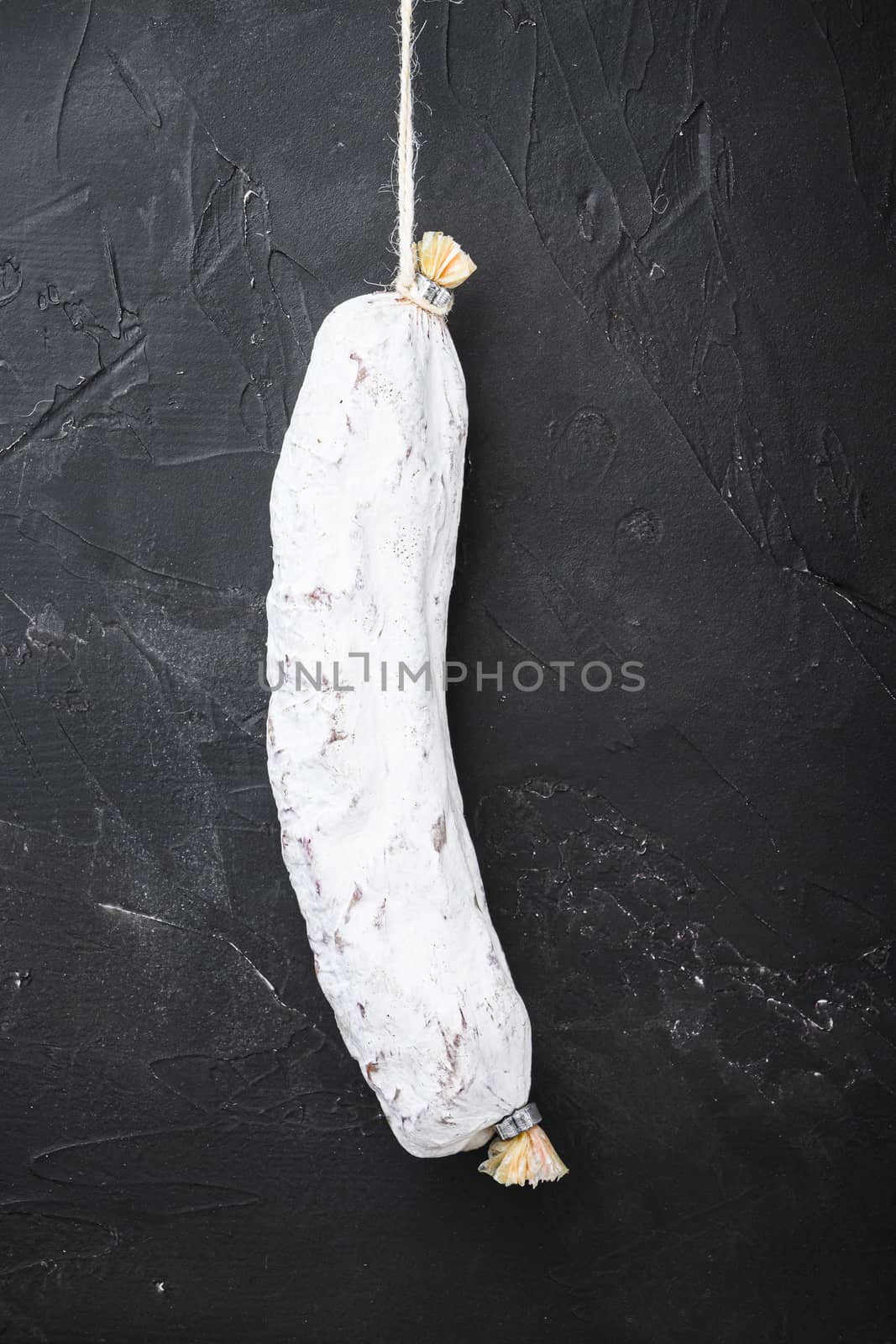 Salchichon, spanish salami sausage on black textured background.