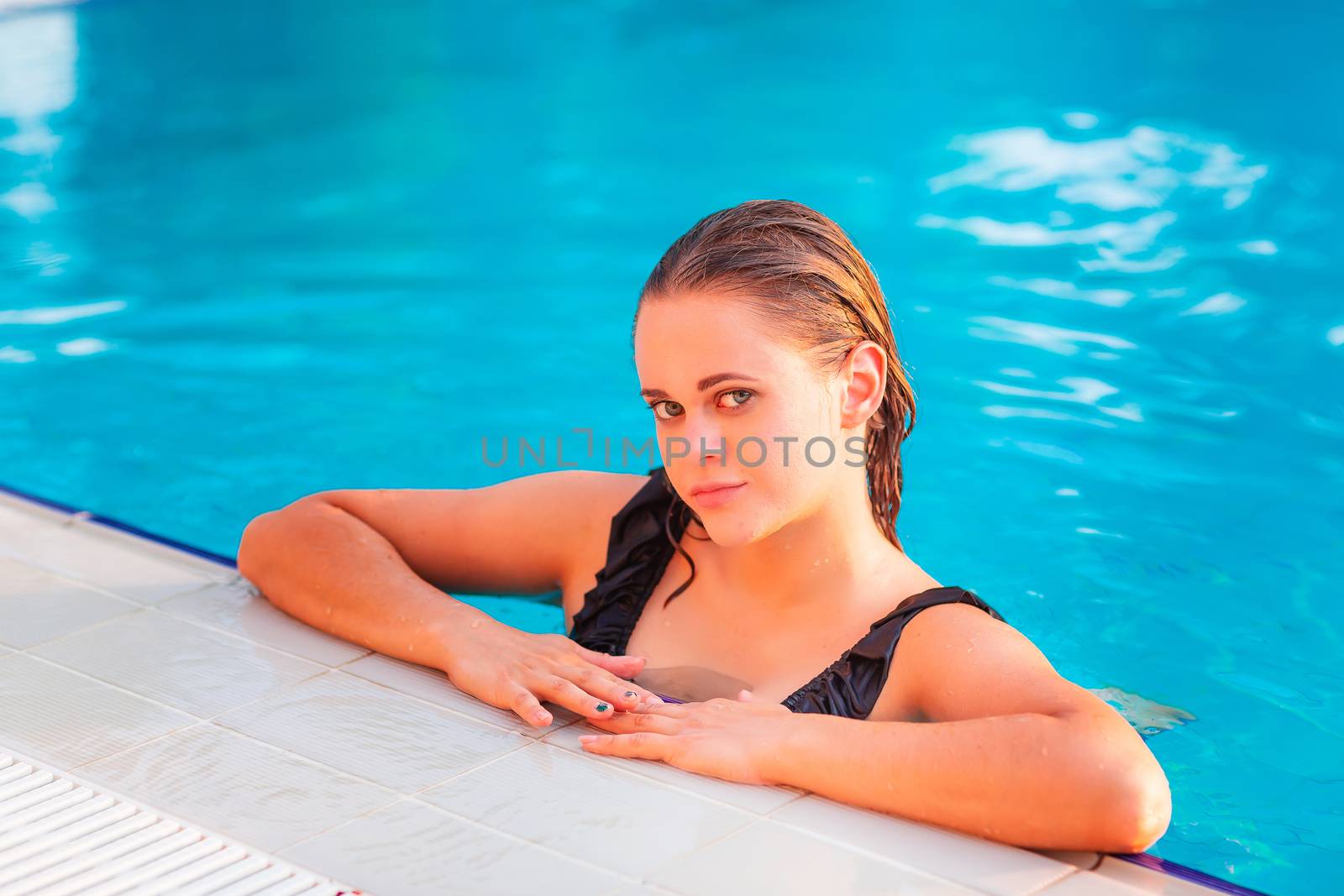 Young beautiful girl in black swimsuit in the pool posing