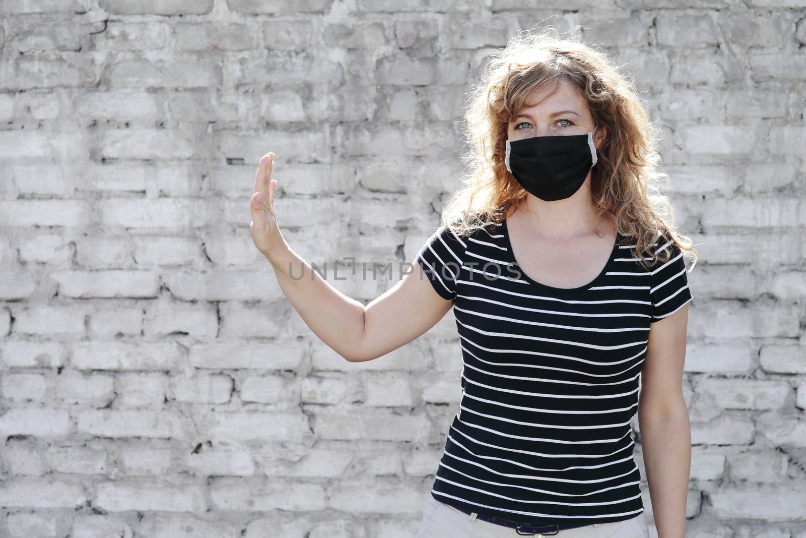 Portrait of a Girl in a protective mask, free space for text. Social distancing. White brick wall in the background. Shows stop by hand