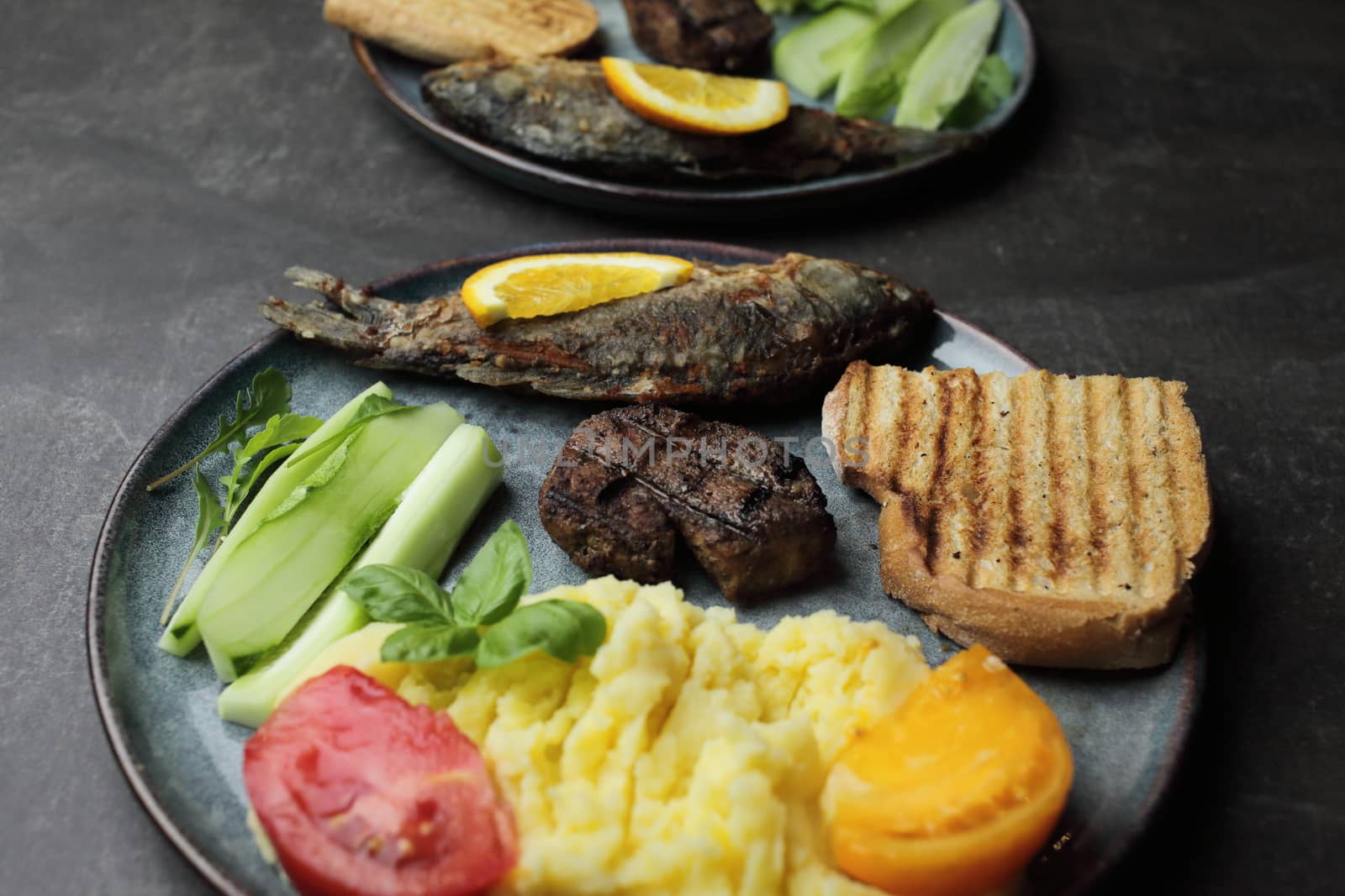 Fried fish, meat steak and vegetables on a plate. Concrete gray countertop. High quality photo