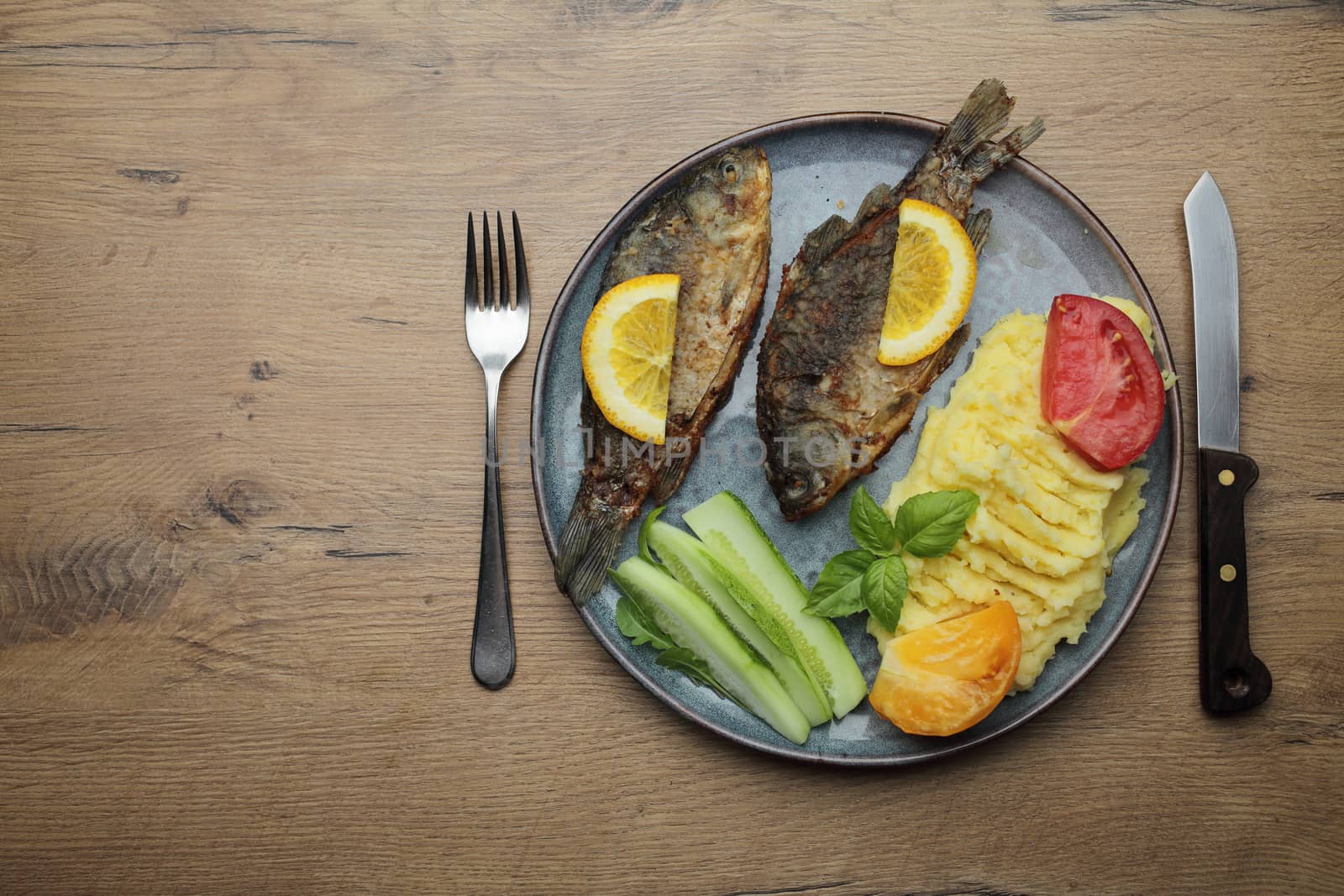 Fried fish and vegetables on a plate. On a wooden table by selinsmo