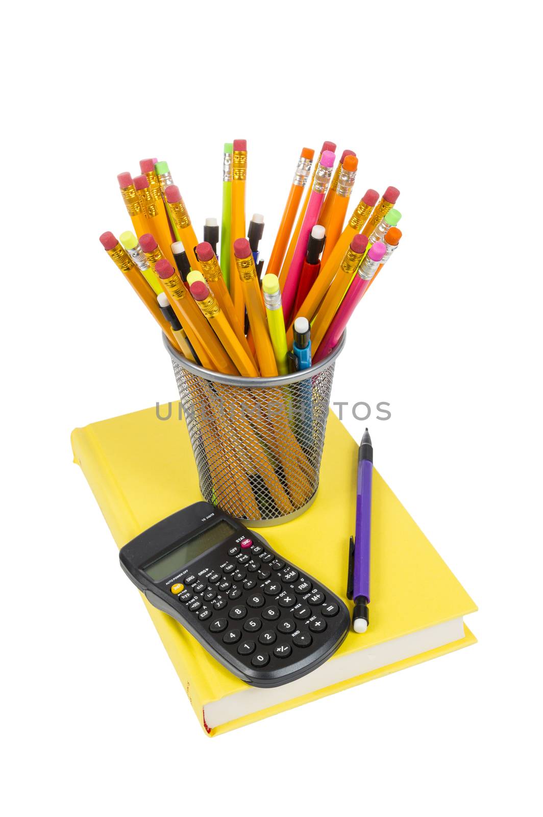Vertical shot of colorful pencils of different kinds inside a pencil holder and resting on a brightly colored yellow book with calculator on top of book as well. Isolated on white background.