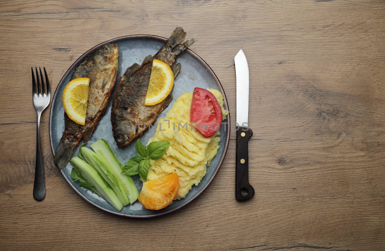Fried fish and vegetables on a plate. On a wooden table. High quality photo