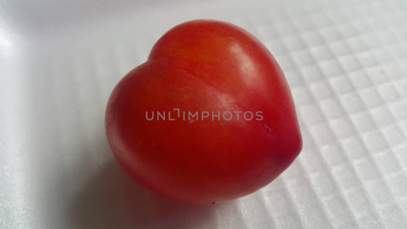 Closeup view of red plum on a white grey background. Freshly harvested plum making heart shape appearance in the view from angle.