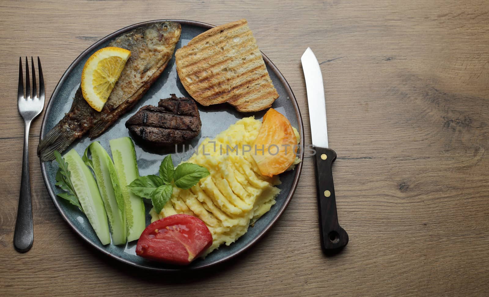 Fried fish, meat steak and vegetables on a plate. On a wooden table. High quality photo