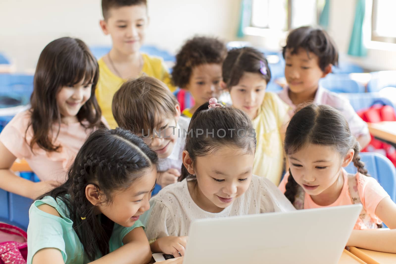 Happy children watching the laptop and discussing in the classroom by tomwang