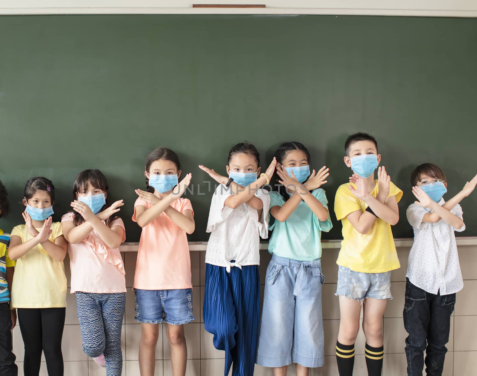 Group of diverse young students wear mask and showing stop sign gesture in classroom by tomwang