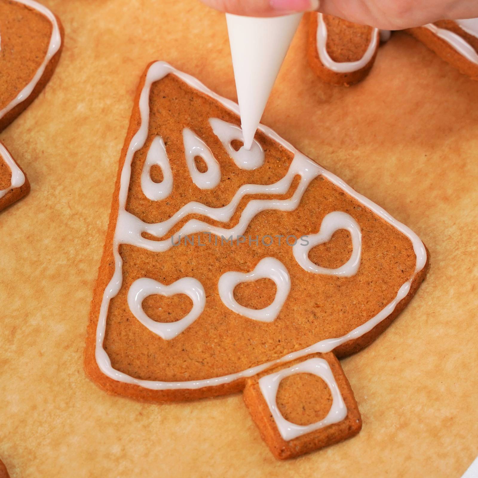 Young woman is decorating Christmas Gingerbread House cookies biscuit at home with frosting topping in icing bag, close up, lifestyle.