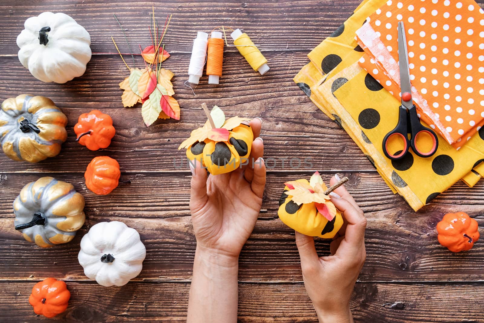 Halloween concept. Woman hands holding DIY textile pumpkins craft over wooden background top view flat lay