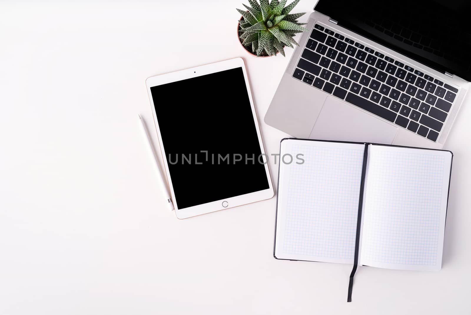 Modern white table with a laptop, tablet and blank notebook. Top view, flat lay, overhead view