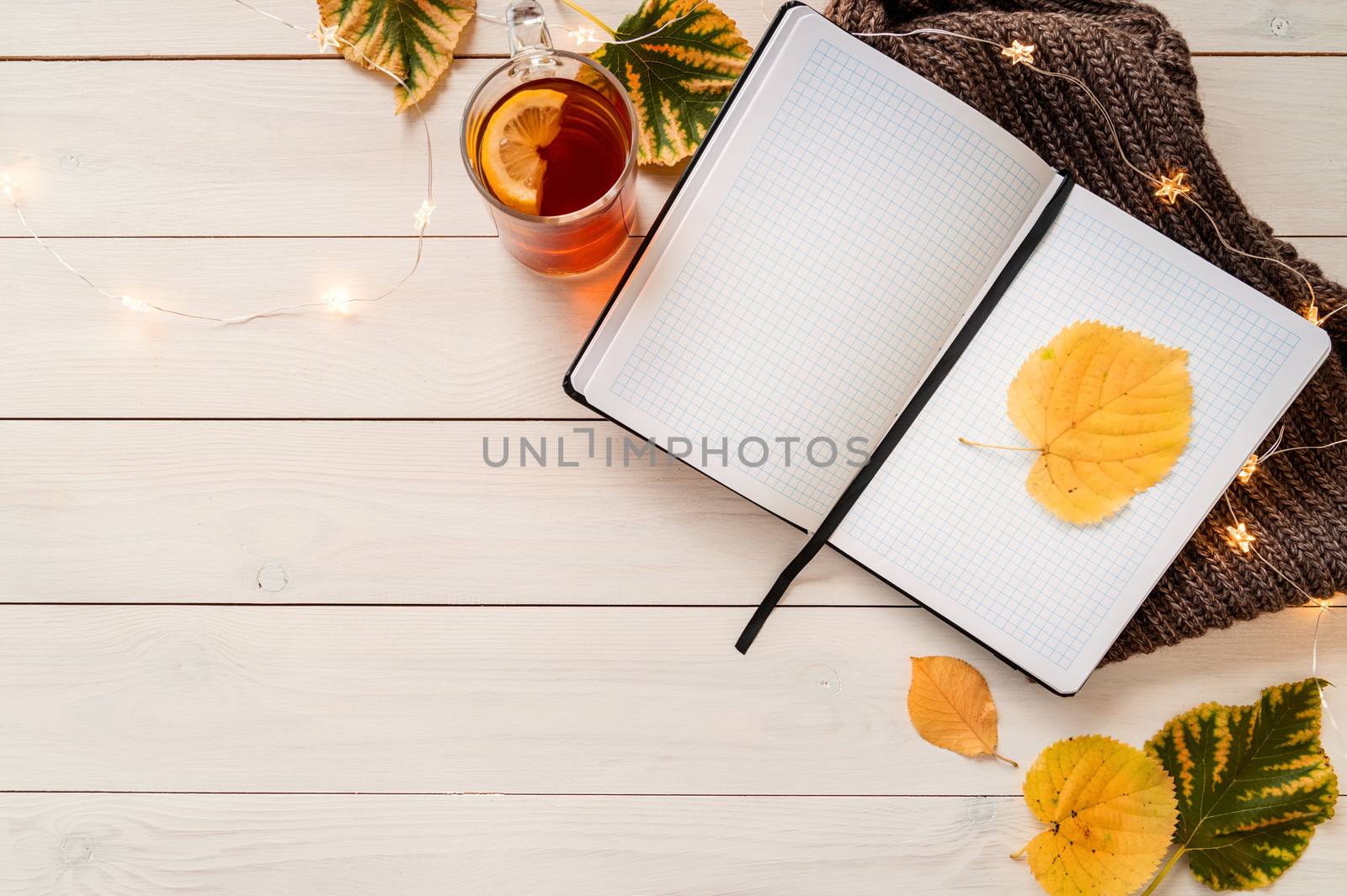 Autumn composition. Workspace with notebook, cup of lemon tea, autumn leaves and fairy lights. Top view, flat lay. by Desperada