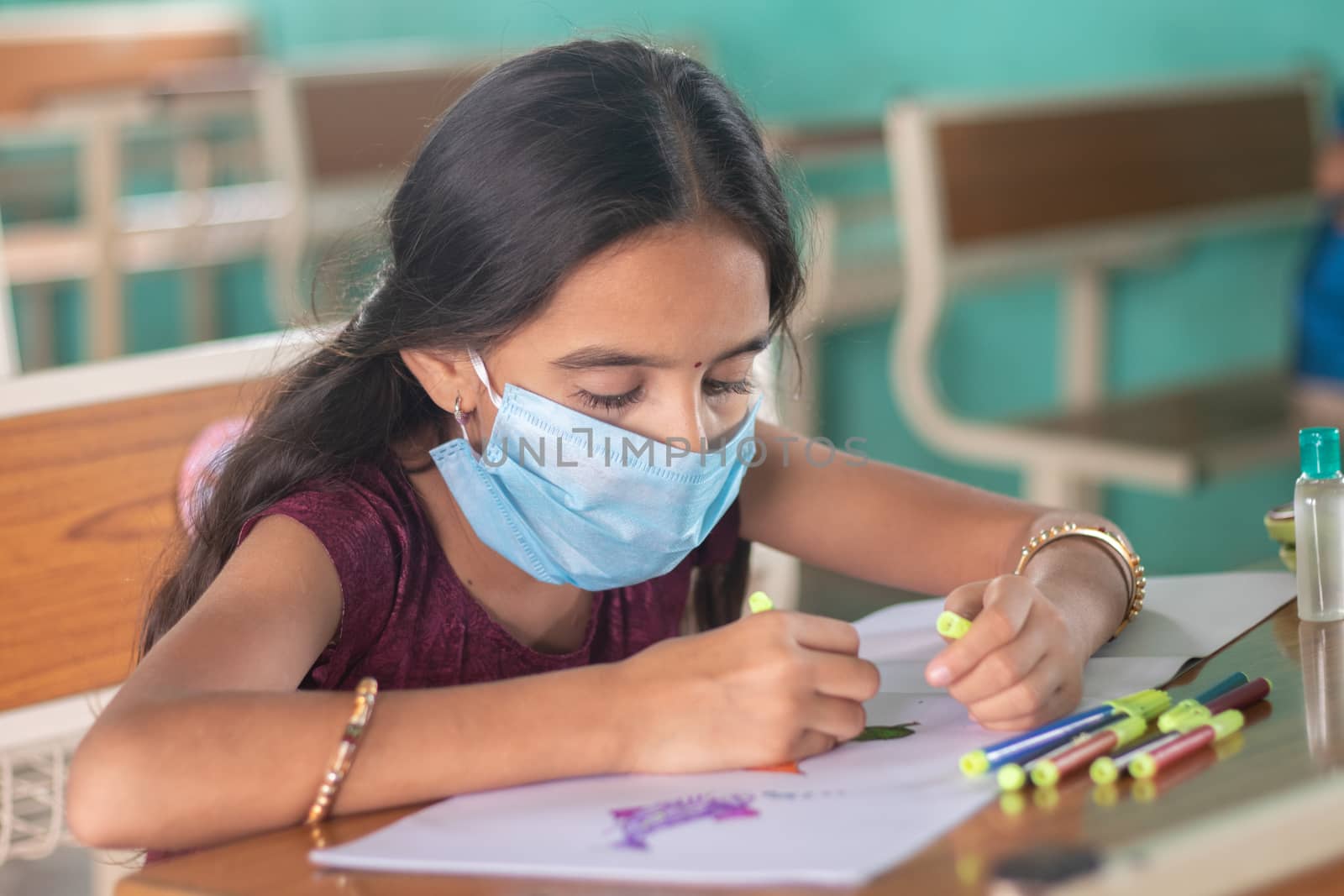 Young girl kid in medical mask busy in drawing sketch at classroom - Concept of safety masures at school due to coronavirus or covid-19 pandemic. by lakshmiprasad.maski@gmai.com