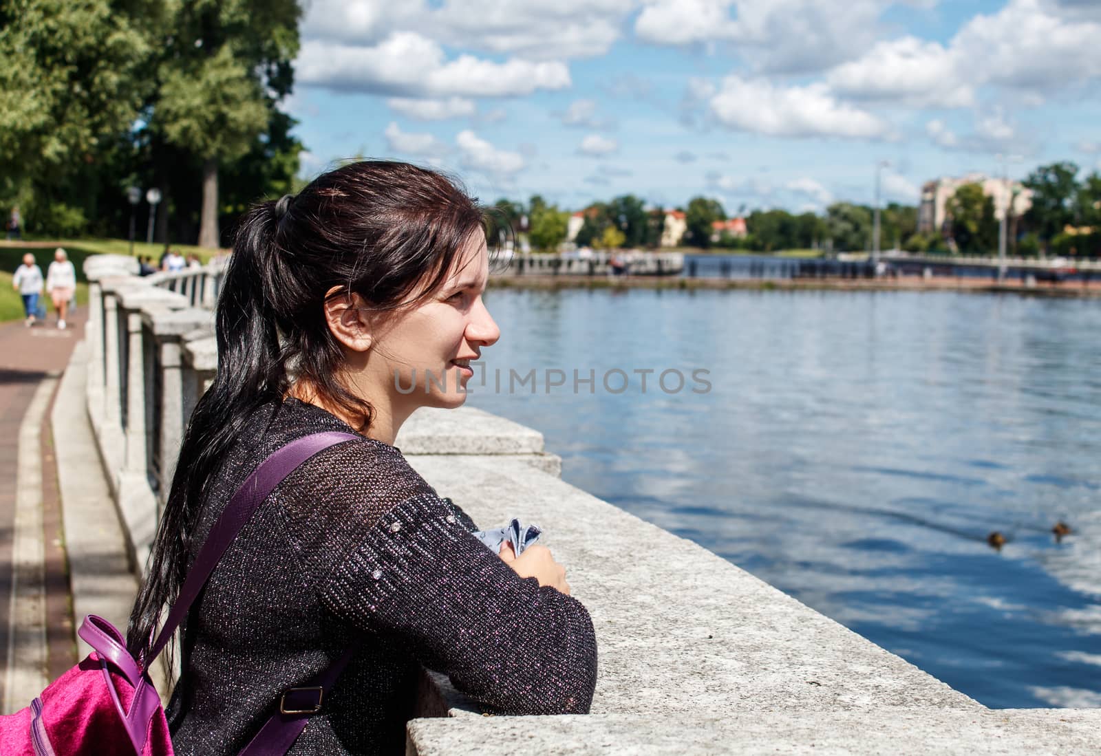 young brunette girl looking at the lake in the city park on sunny summer day