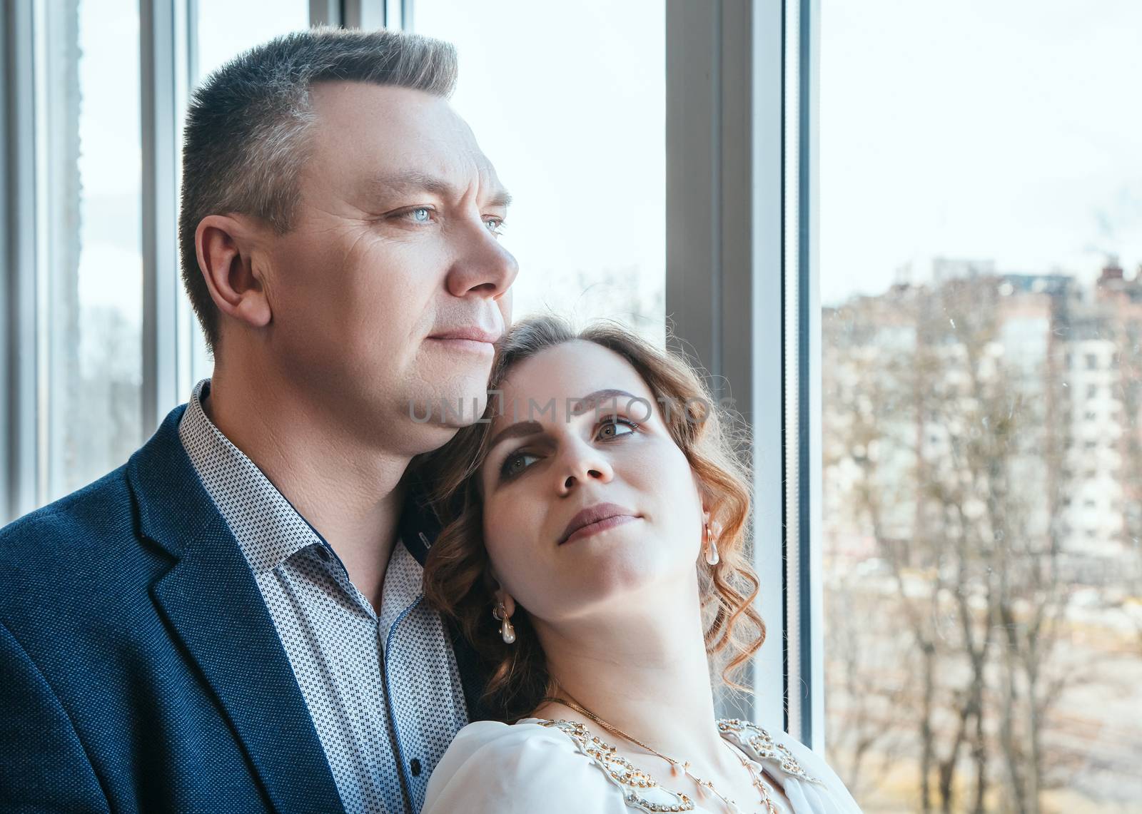 married couple standing by the window indoor in their home