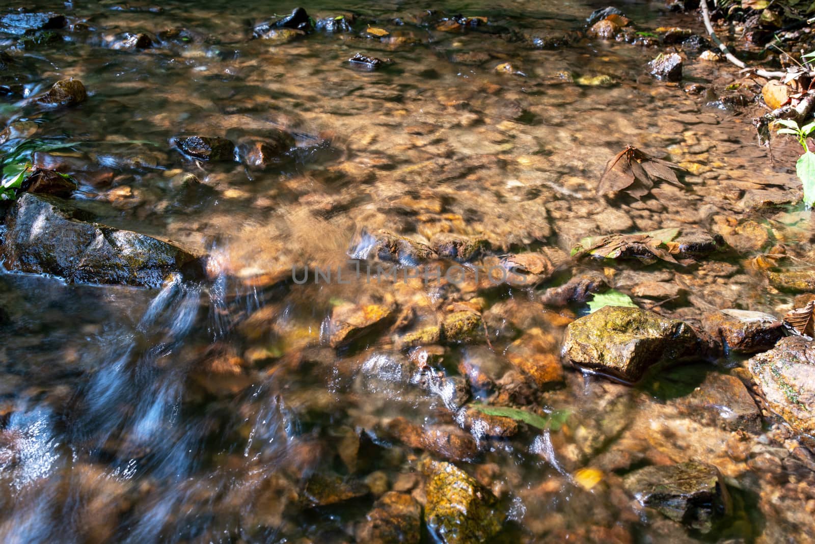 Long exposure surreal abstract view of a flowing woodland stream with colorful stones and reflected blue sky. Full frame tranquil nature image in natural light with copy space.