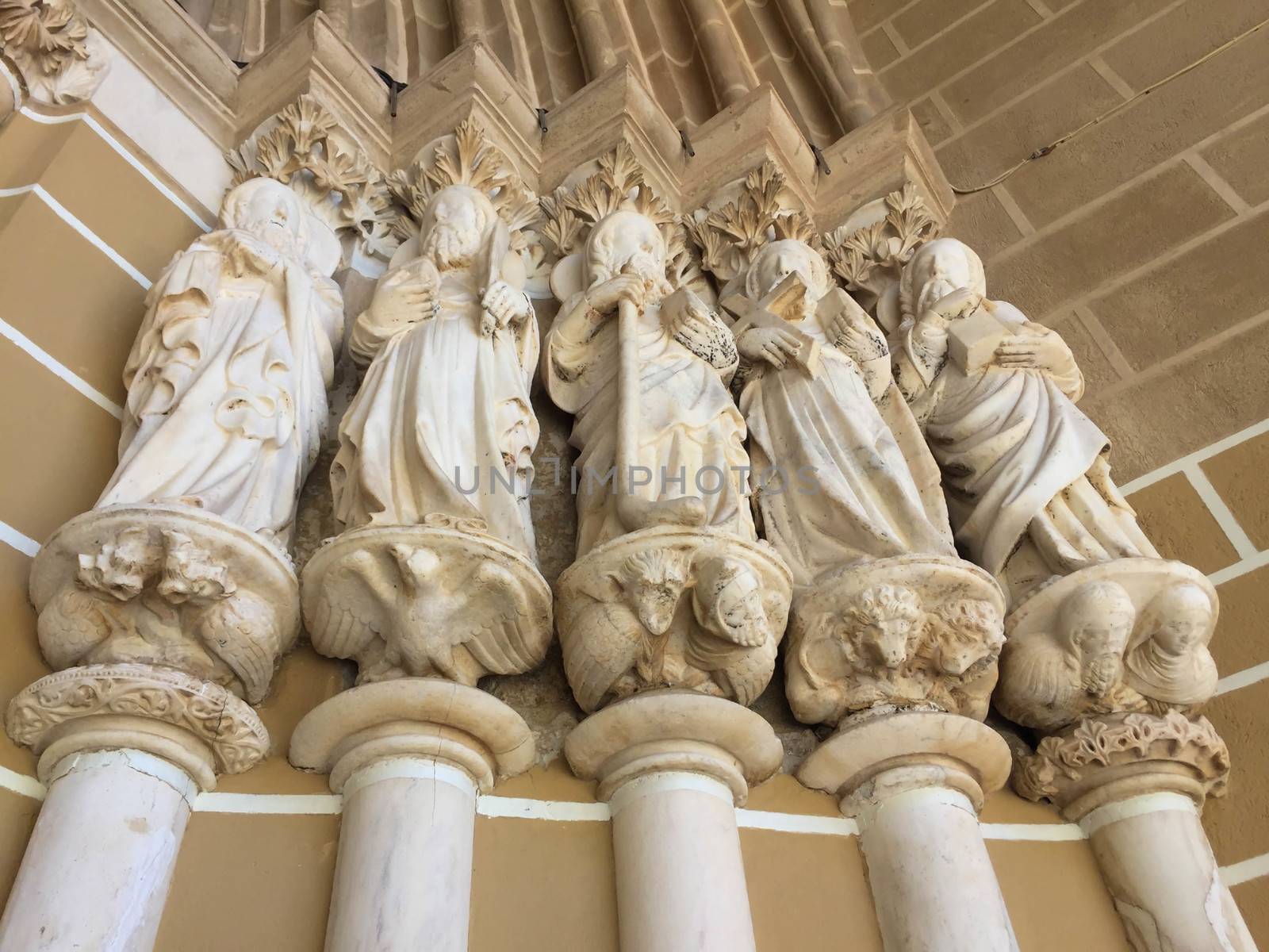 Fourteenth century statues of five apostles rise on columns at the entrance to the cathedral in Évora, Portugal. Low-angle image shot in natural light shows lovely color and detail of figural bases.