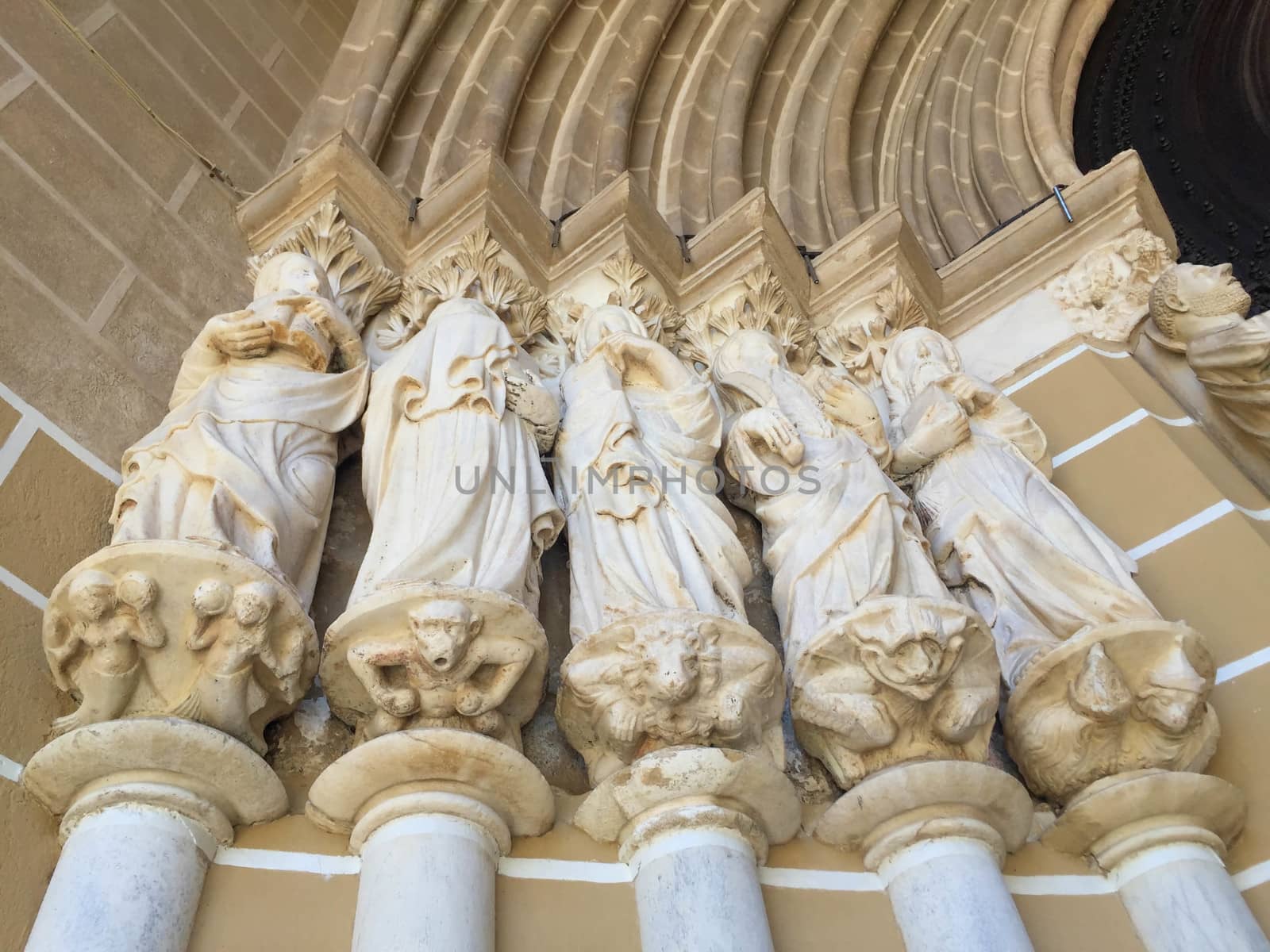 Fourteenth century statues of five apostles rise on columns at the entrance to the cathedral in Évora, Portugal. Low-angle image shot in natural light shows lovely color and detalil of figural base.