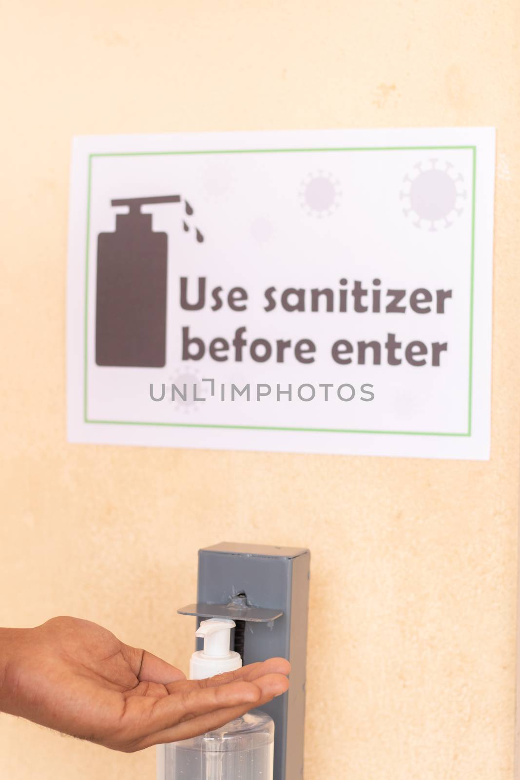 Close up of hands using hand sanitizer below the use sanitizer before enter signage board on wall as safety measure due to coronavirus or covid-19 pandemic.