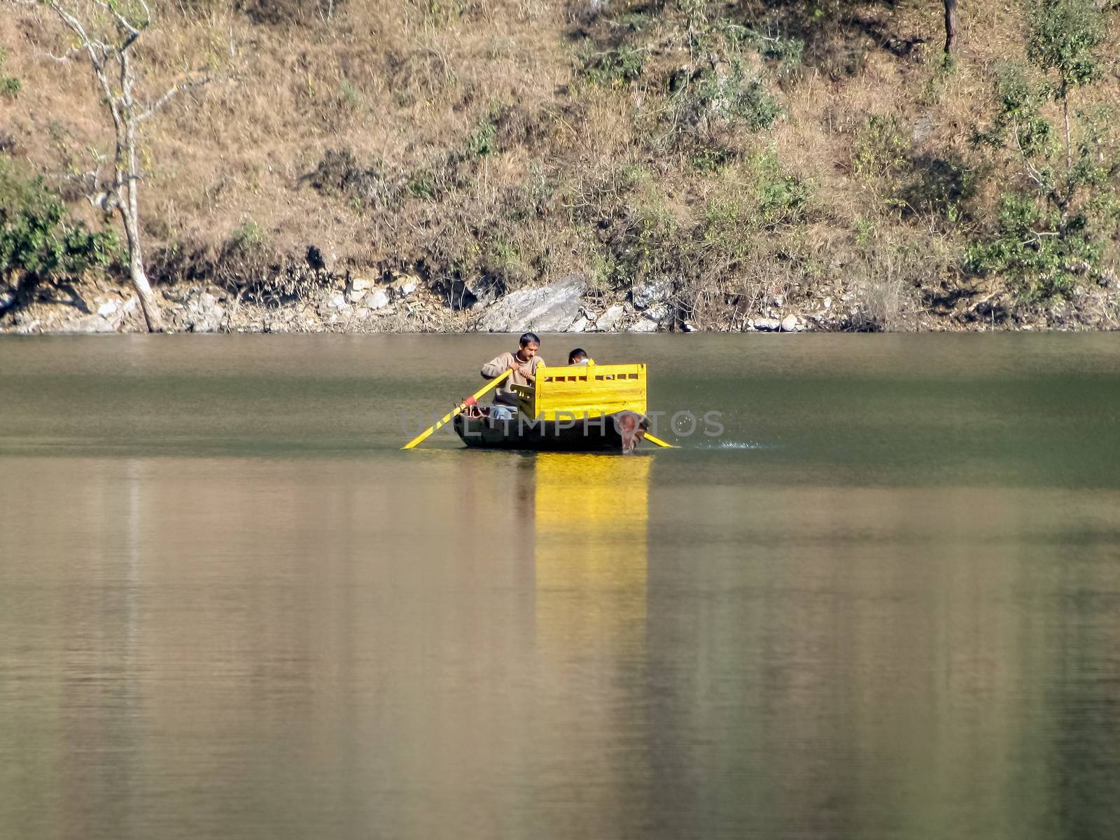Boatman with tourist rowing his small yellow boat in waters of Bhimtal lake. by lalam