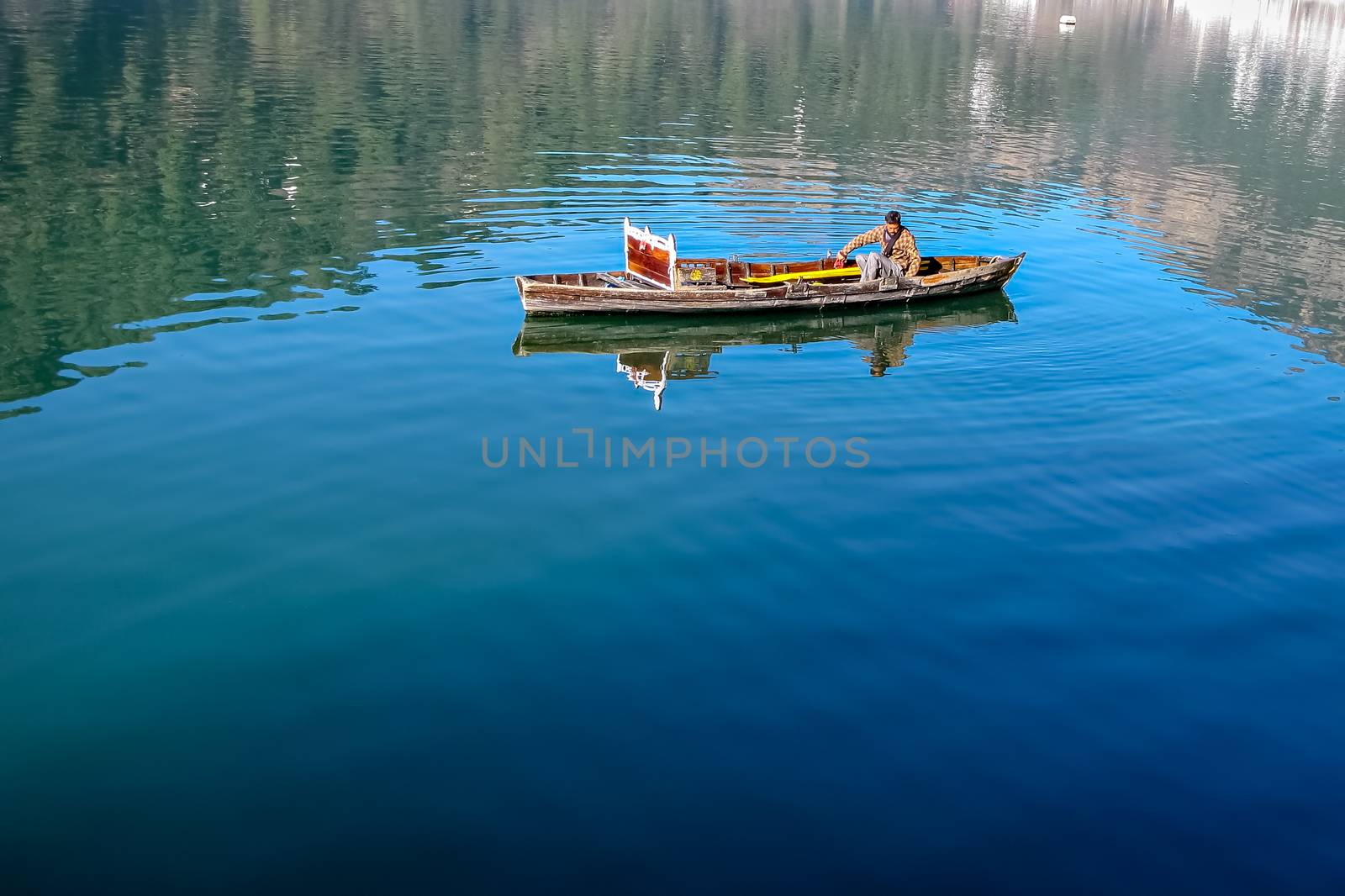 Boatman rowing his small boat in blue waters of Bhimtal lake. by lalam