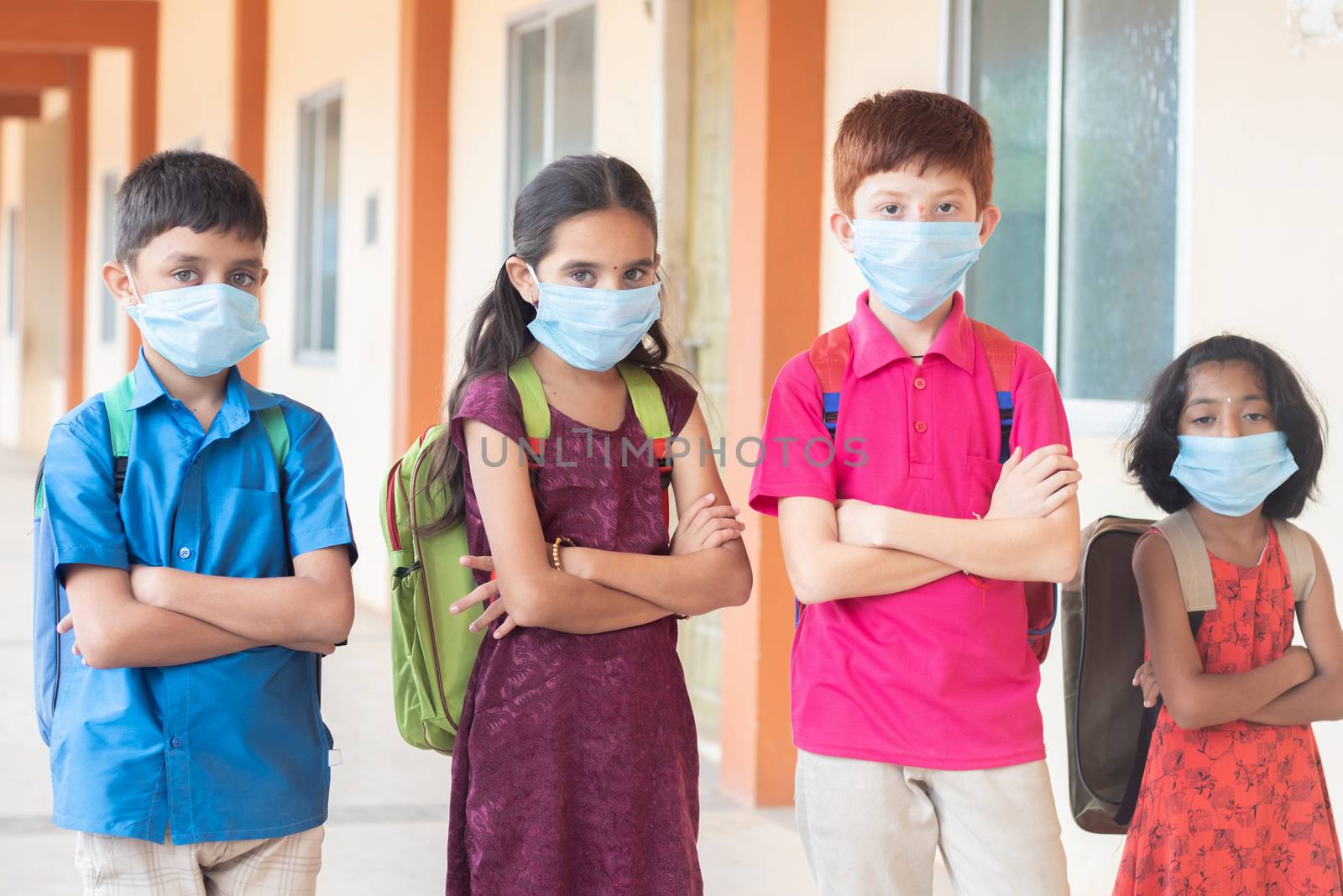 Children in medical mask with school backpack standing with arms crossed by looking to the camera- Concept of back to school and reopen