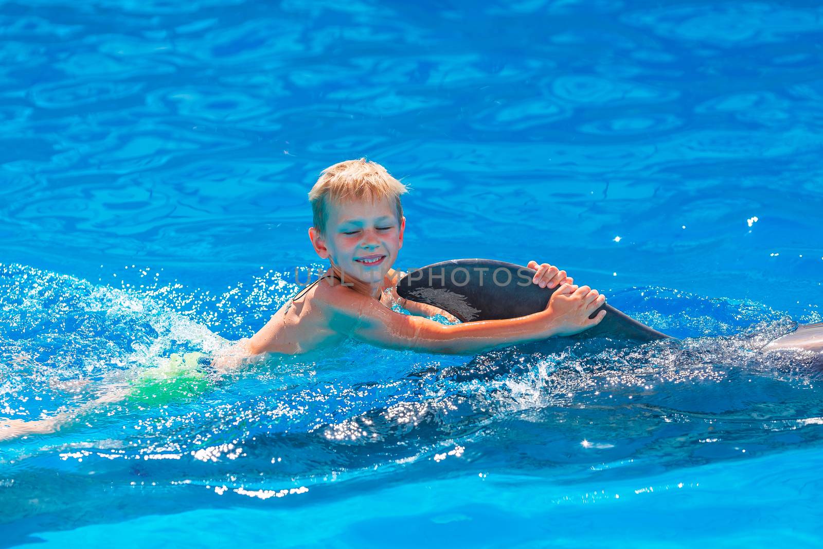 Happy little boy swimming with dolphins in Dolphinarium. Swimming, bathing and communication with dolphins.