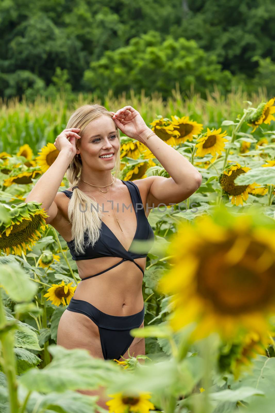 A gorgeous blonde model poses outdoors in a field of sunflowers while enjoying a summers day