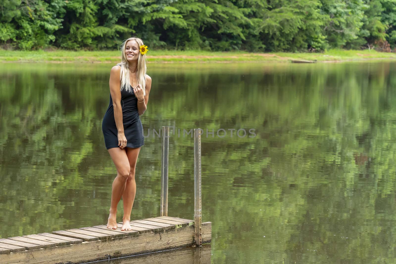 A gorgeous blonde model poses outdoors near a pond while enjoying a summers day
