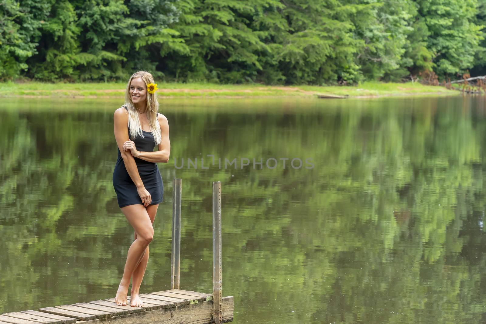 A gorgeous blonde model poses outdoors near a pond while enjoying a summers day