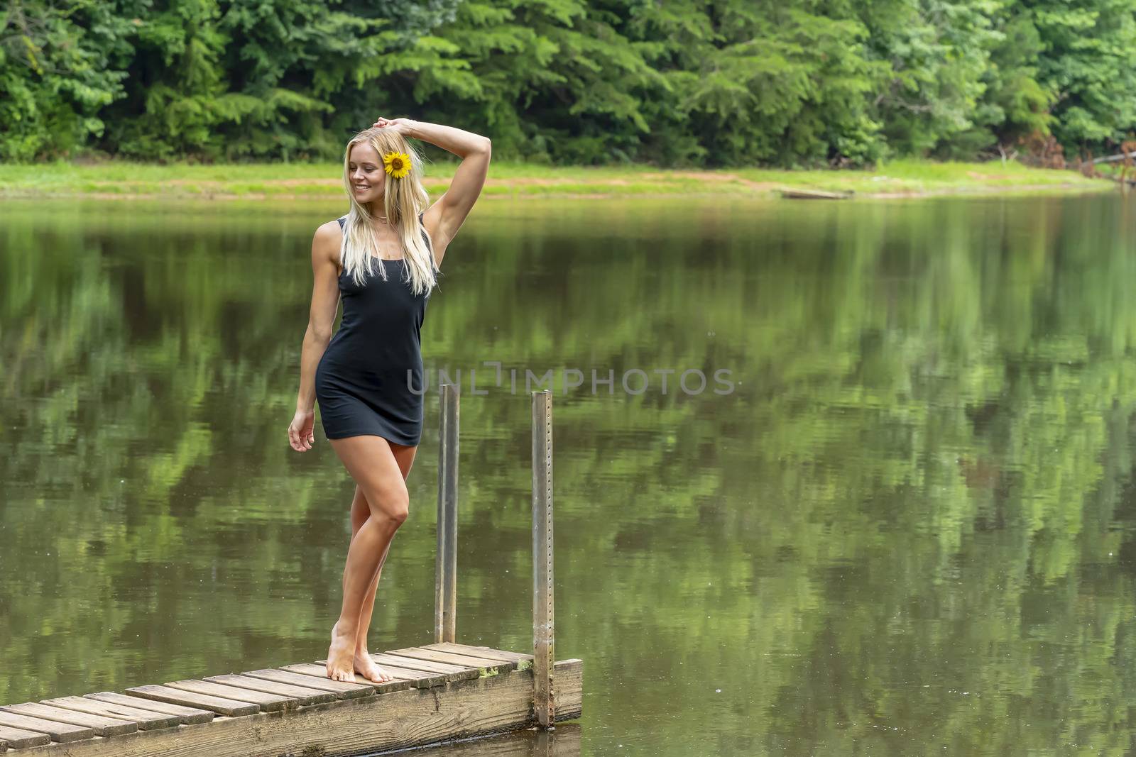 A gorgeous blonde model poses outdoors near a pond while enjoying a summers day
