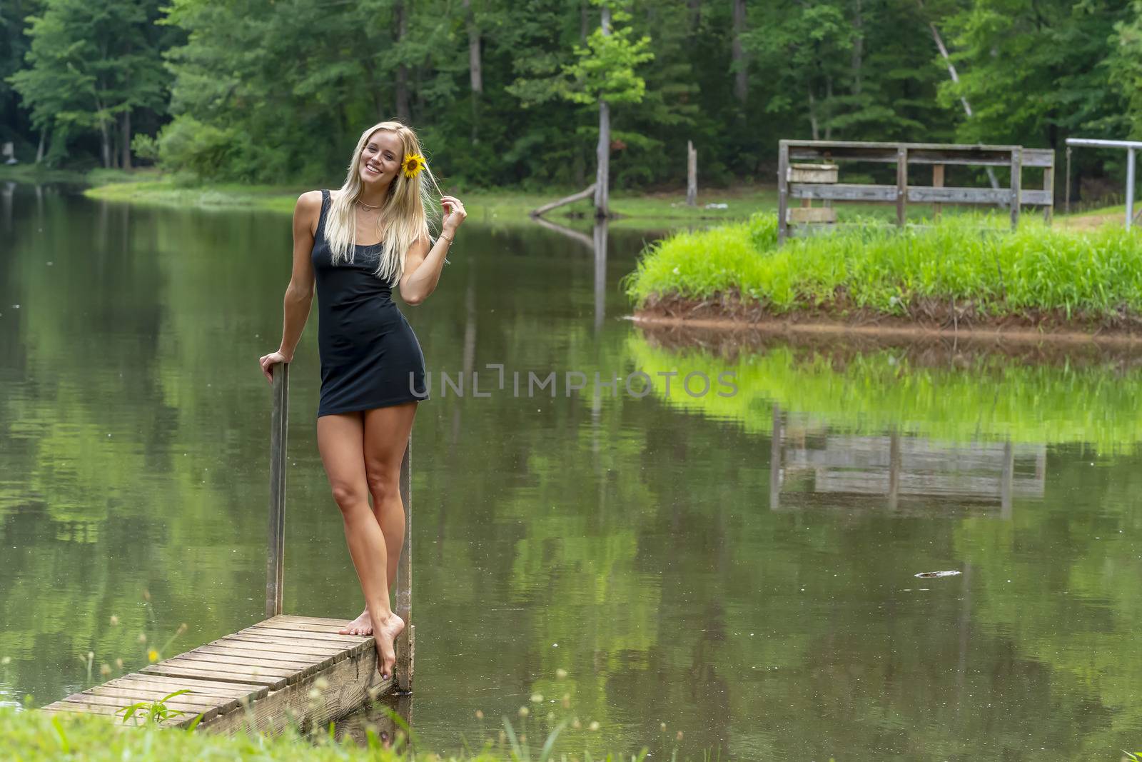 A gorgeous blonde model poses outdoors near a pond while enjoying a summers day