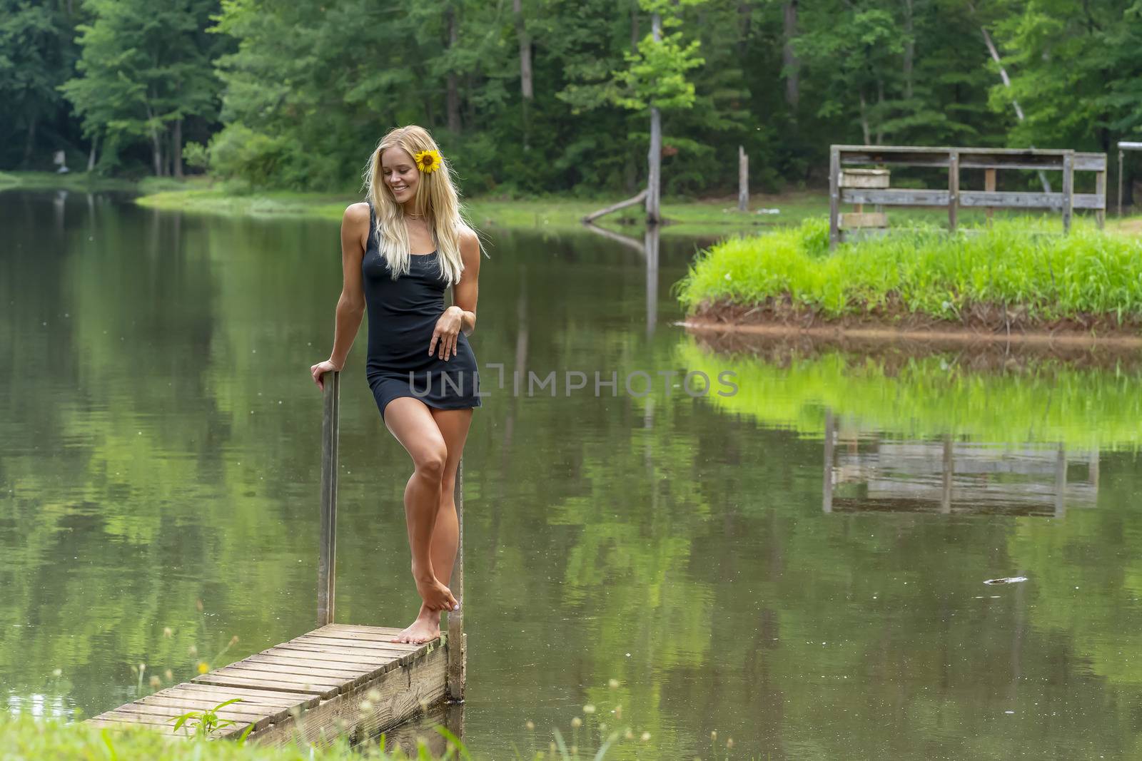 A gorgeous blonde model poses outdoors near a pond while enjoying a summers day