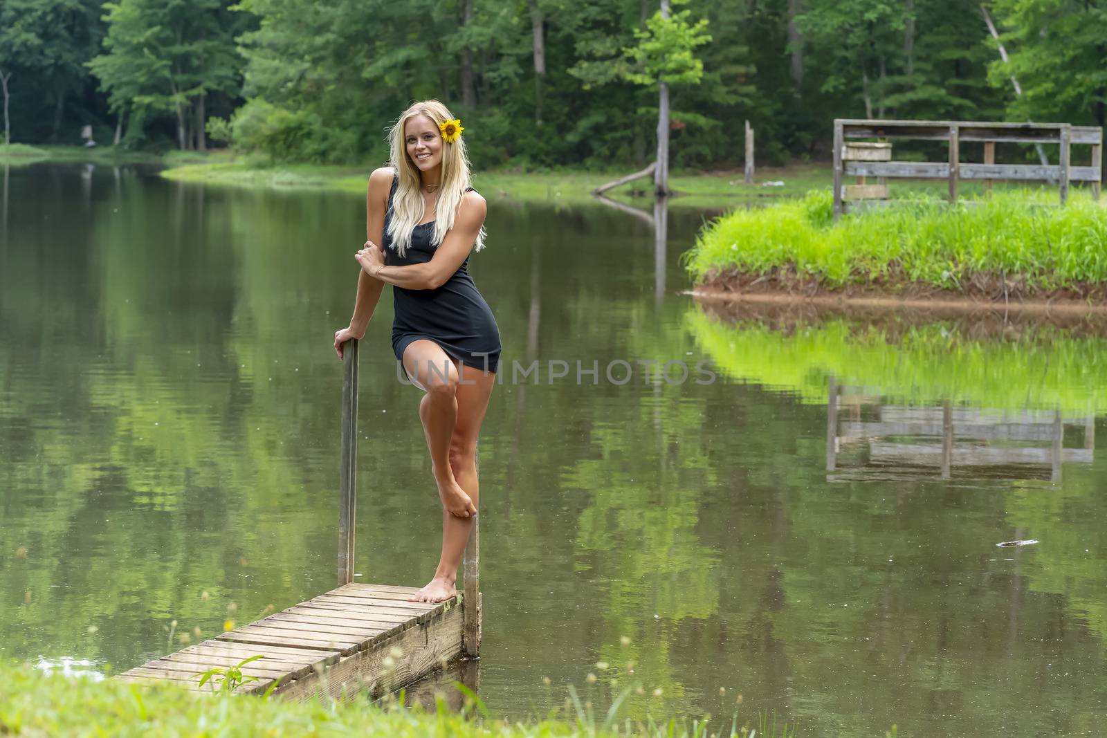 A gorgeous blonde model poses outdoors near a pond while enjoying a summers day