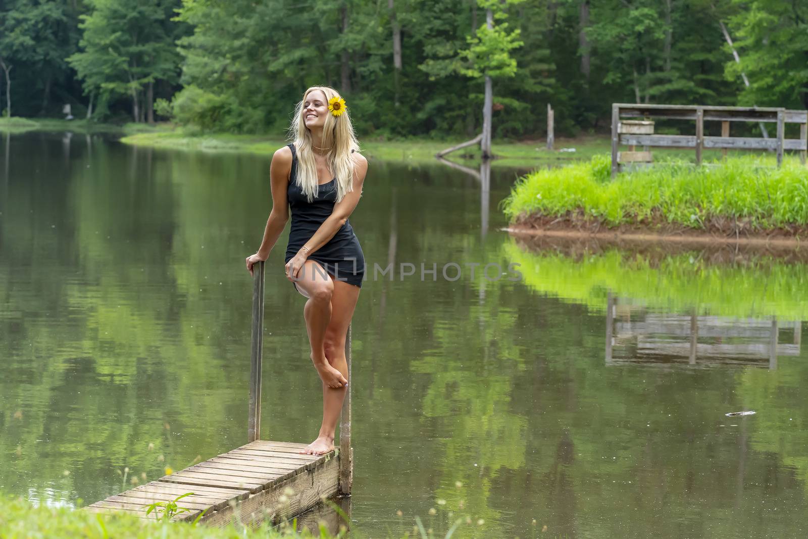 A gorgeous blonde model poses outdoors near a pond while enjoying a summers day