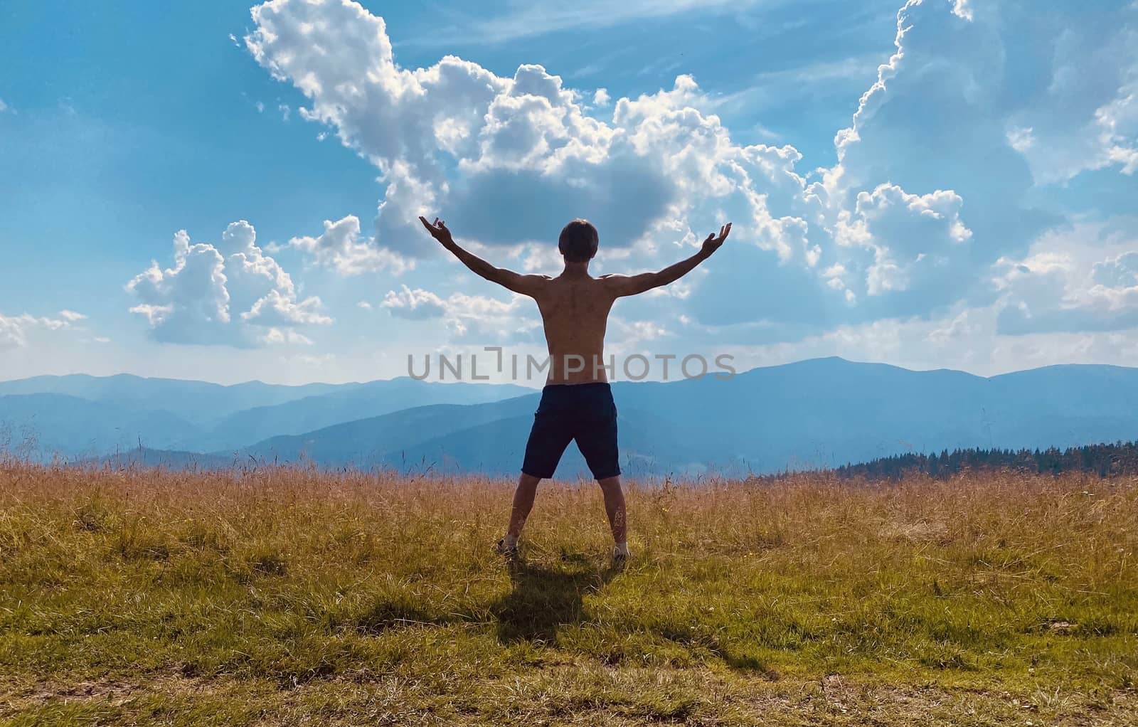 happy young man with arms raised	 among mountains by Boiko